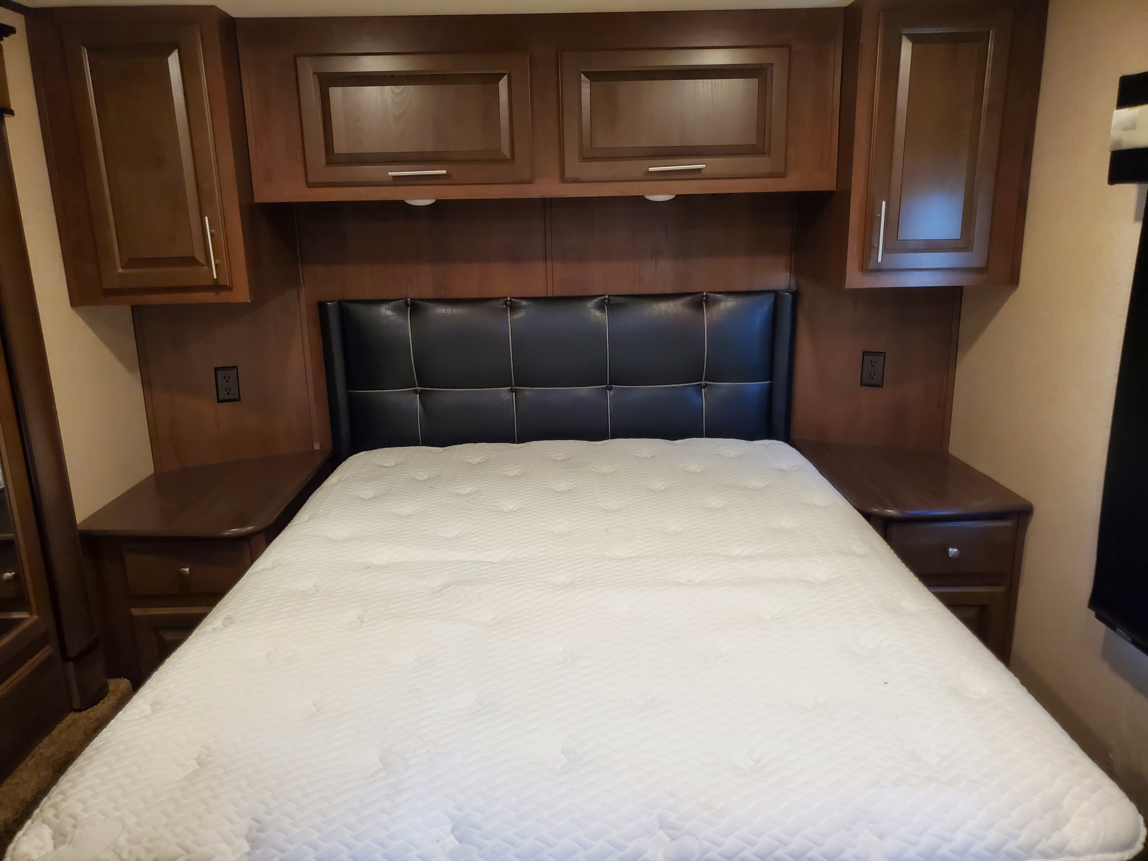 RV rental interior: A cozy bedroom featuring a large mattress, black headboard, wooden cabinets, and nightstands.. Jayco Seismic Toy Hauler 2015