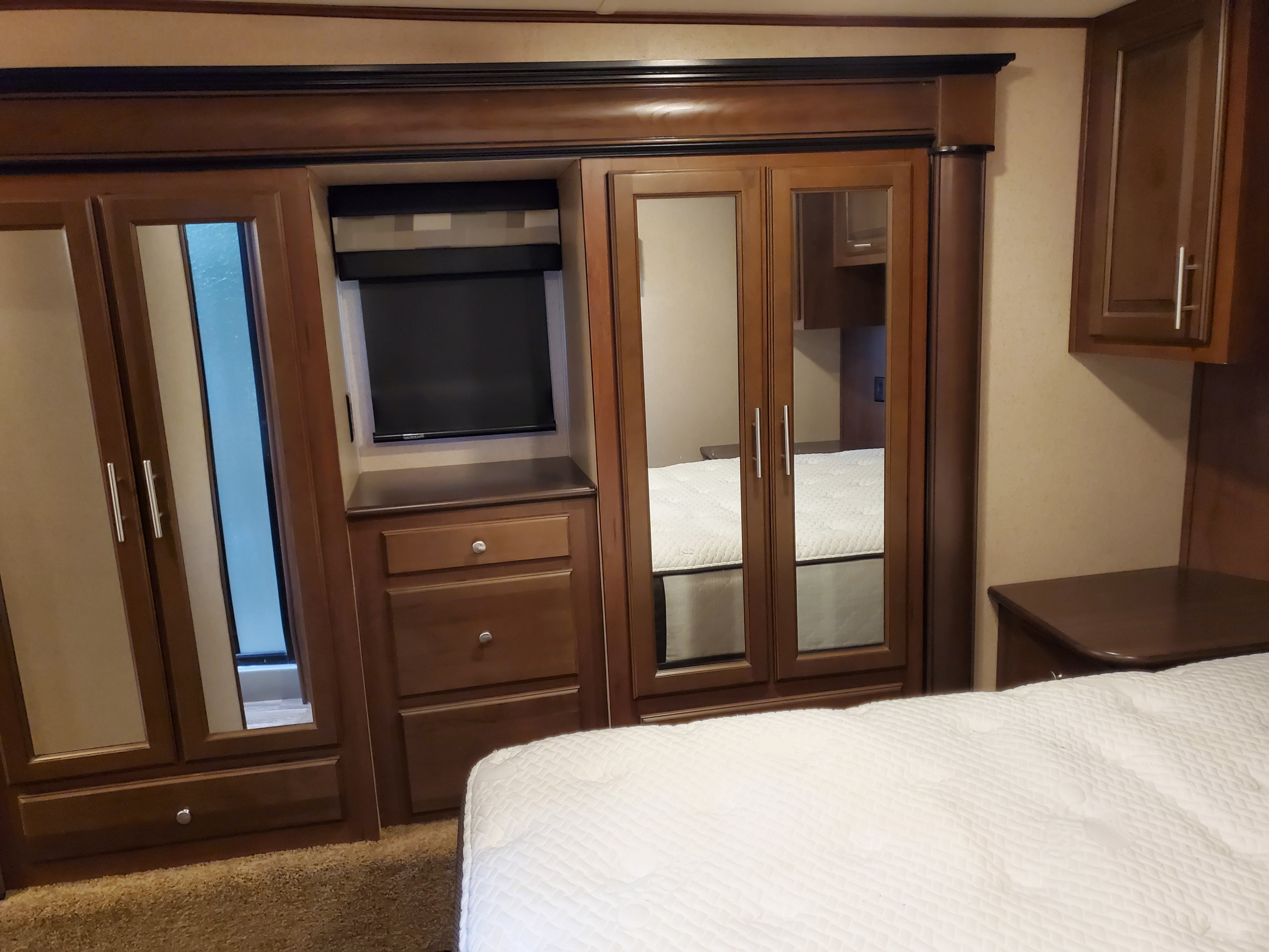 RV rental bedroom interior featuring a comfortable bed, mirrored wardrobes, built-in TV, and wood cabinetry for storage.. Jayco Seismic Toy Hauler 2015