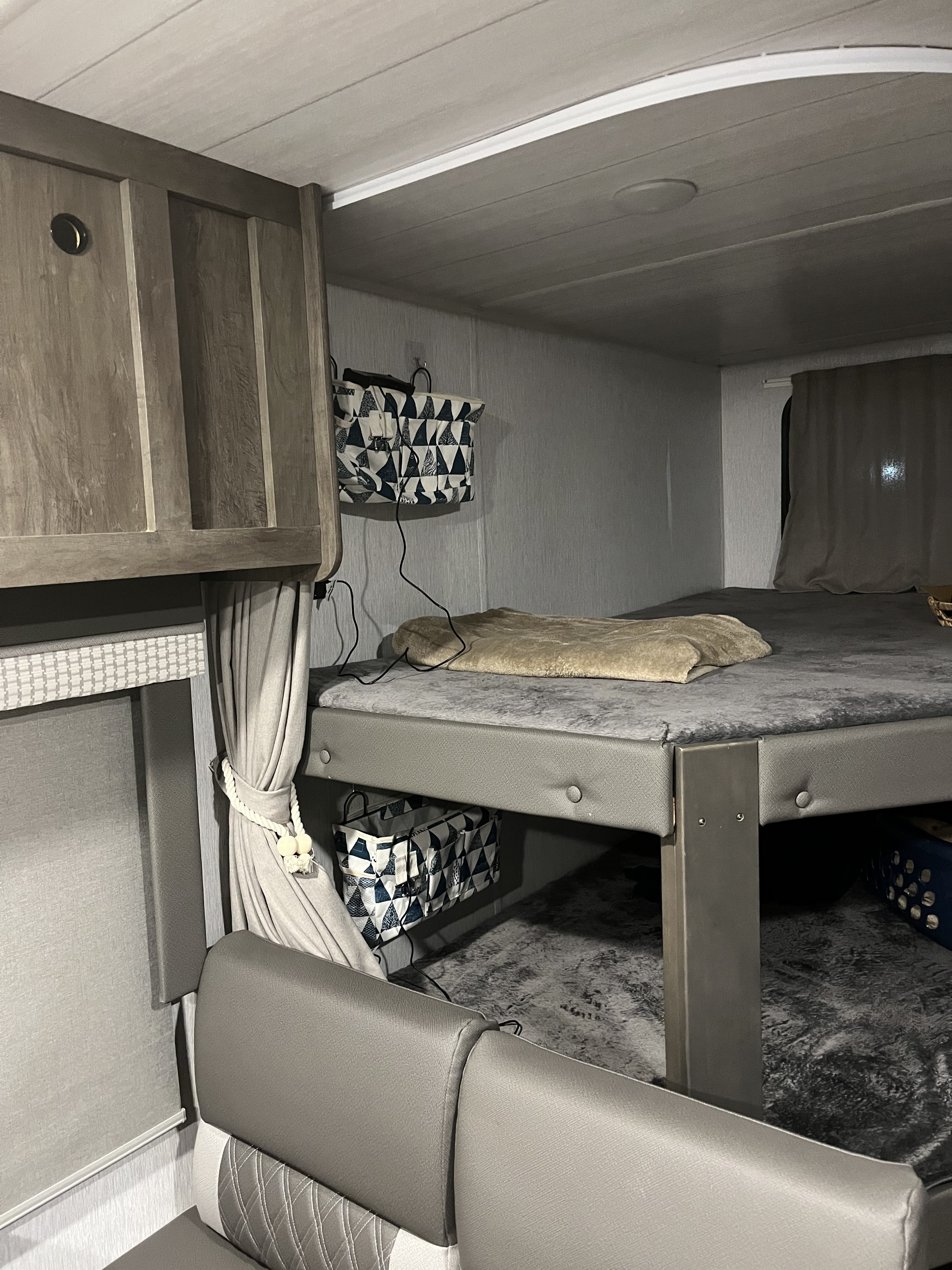 Inside an RV rental: a modern bunk bed with built-in storage, drapes, and cushioned seating below, in grey tones.. Forest River Salem Cruise Lite 2022