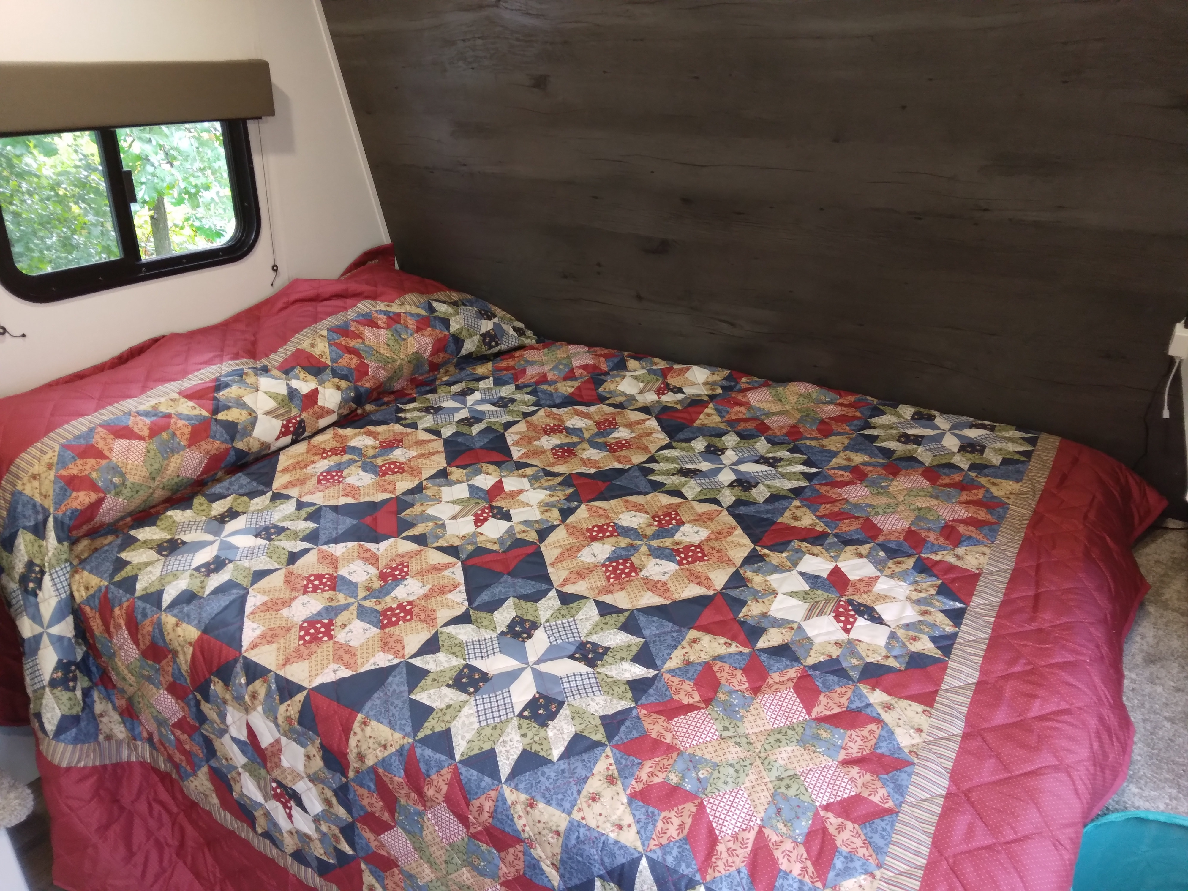 Cozy RV rental bedroom with a vibrant patchwork quilt and window view. Perfect for travel.. Keystone RV Hideout 2022