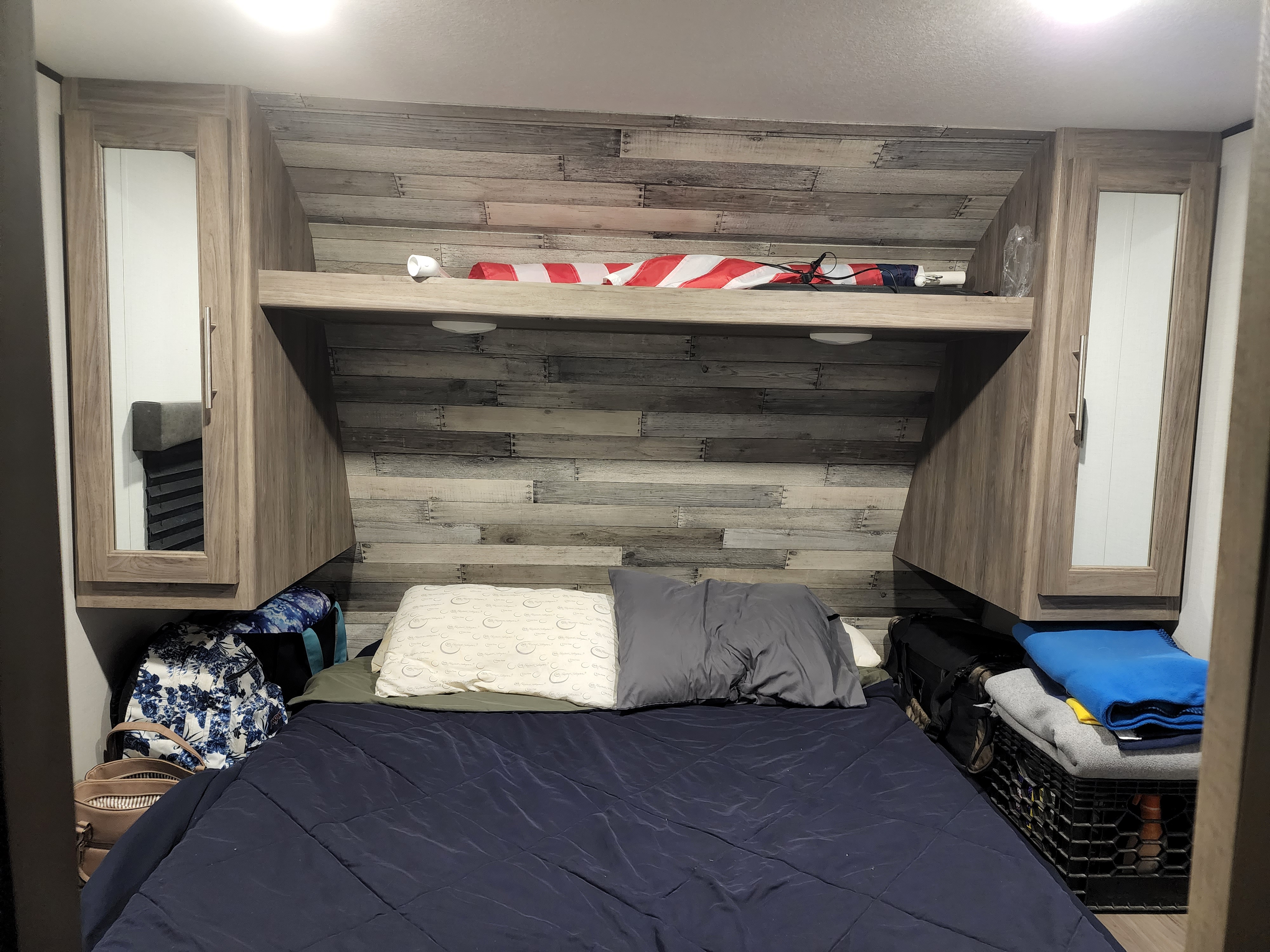 RV rental bedroom: a bed with dark blue comforter, overhead storage, and wood-paneled headboard.. Keystone RV ZR331BH20 2020