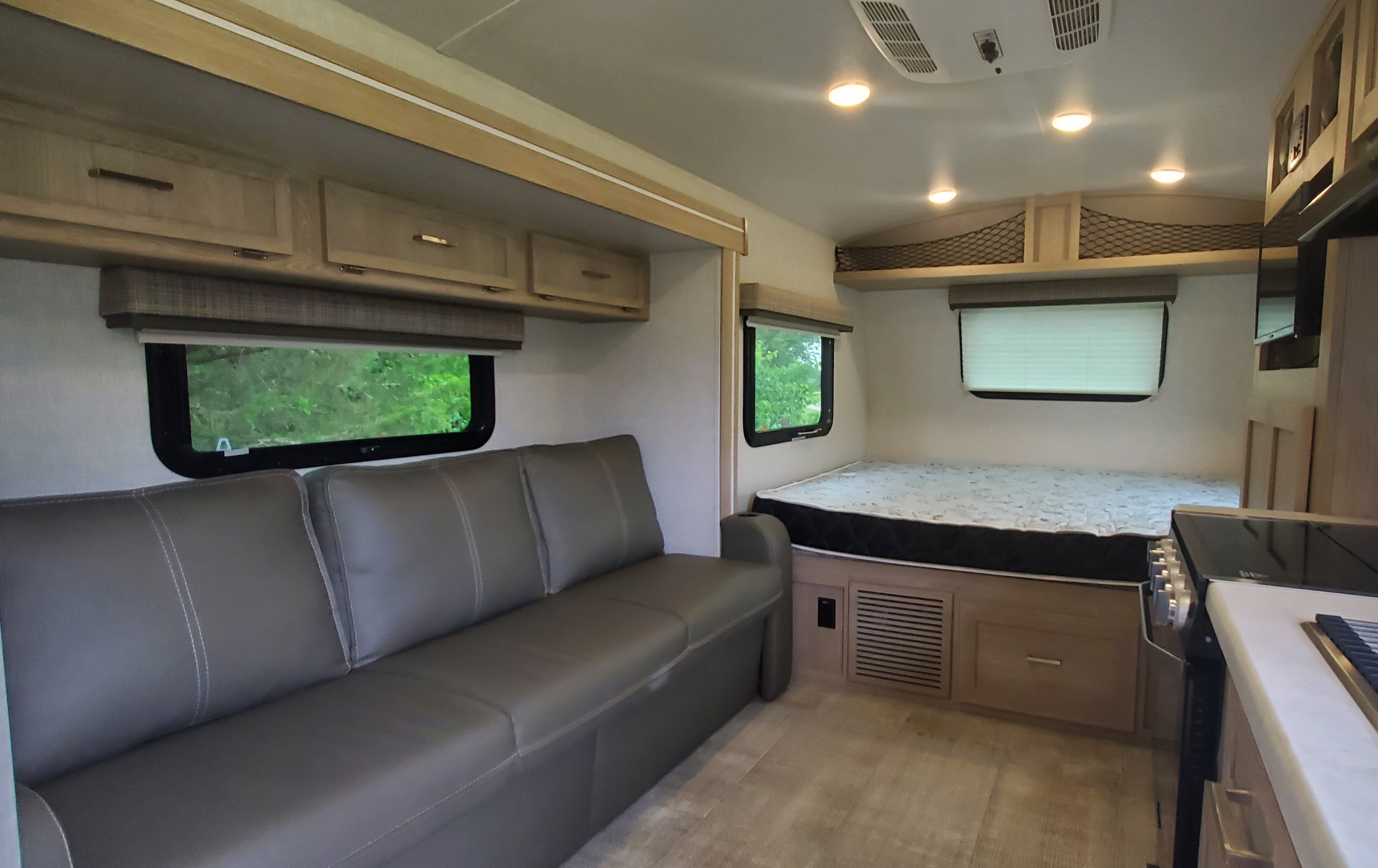 RV rental interior featuring a gray sofa, queen bed with patterned mattress, windows, overhead cabinets, and a kitchen area.. Forest River Flagstaff E-Pro 2021