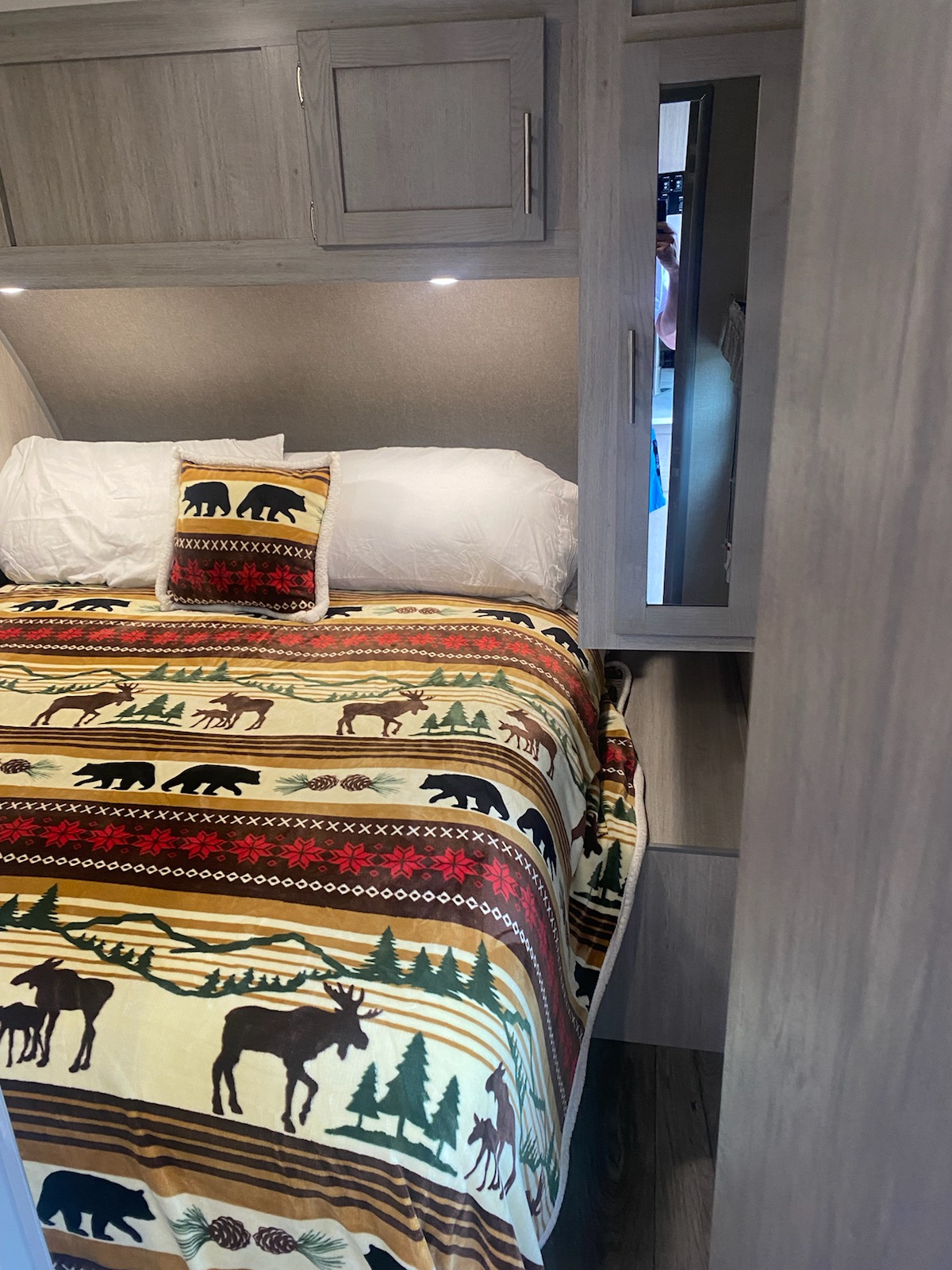 Rustic RV rental bedroom featuring a bed with nature-themed blanket, white pillows, and overhead storage.. Coachmen Catalina Legacy Edition SP3000 2022