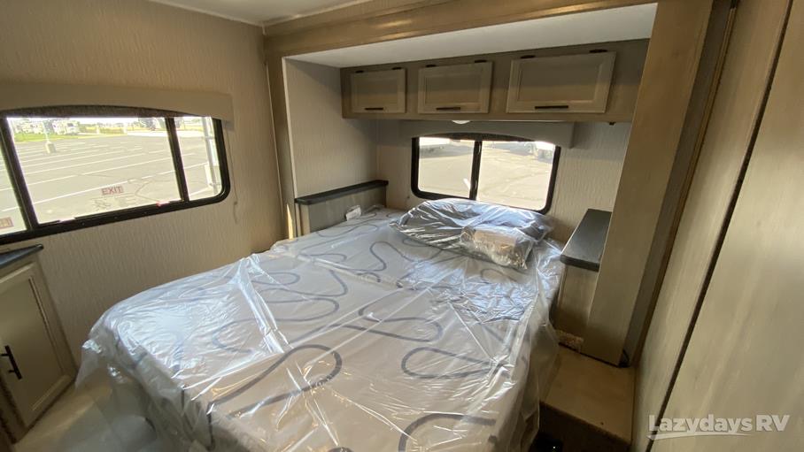 View inside an RV rental's comfortable bedroom, featuring a protected bed, practical overhead cabinets, and twin windows.. Coachmen Freelander 2023