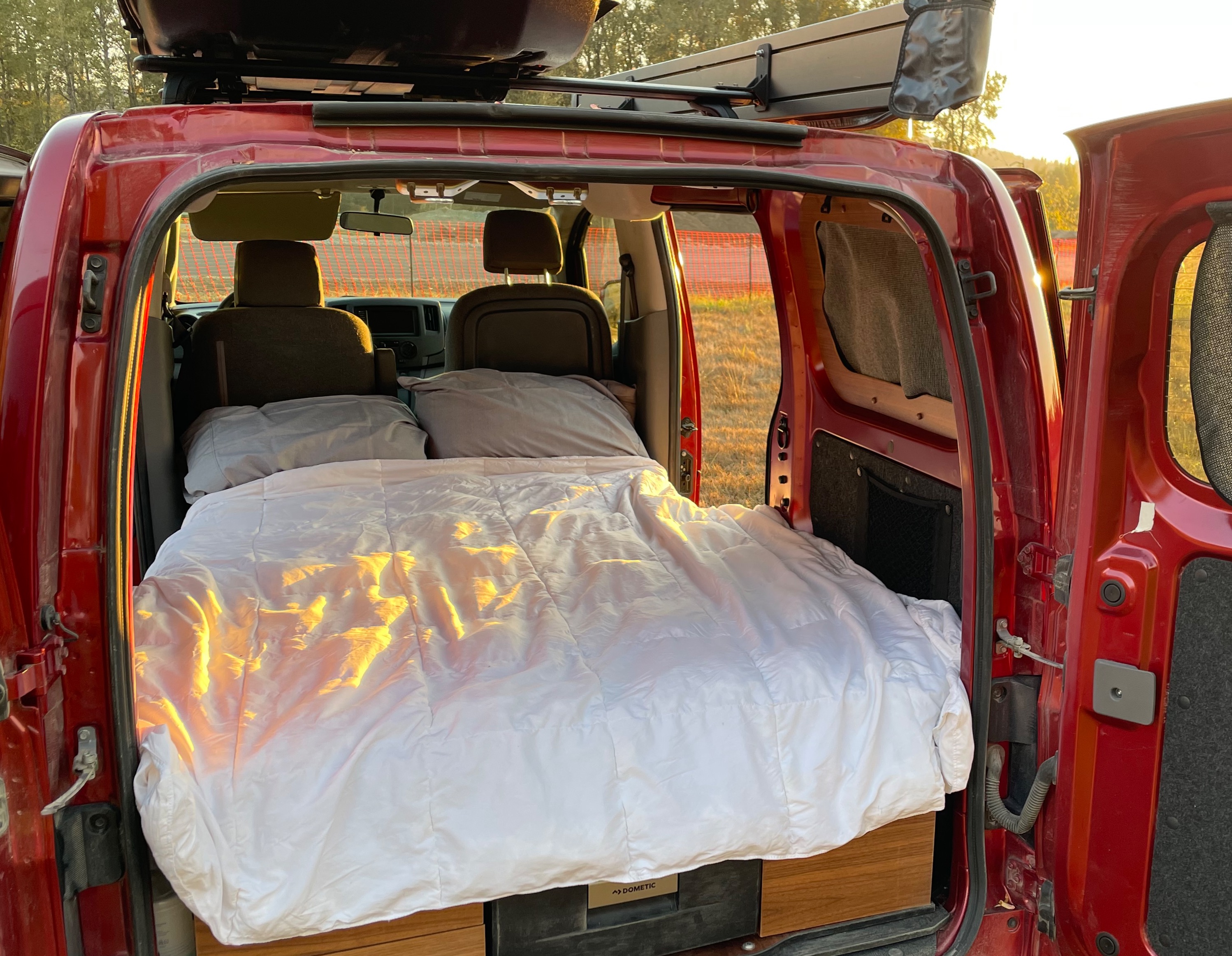 Sleep comfortably in this red **rv rental**. Inside, a cozy bed with white linens awaits your **van life** trip.. Nissan Elgrand 2021