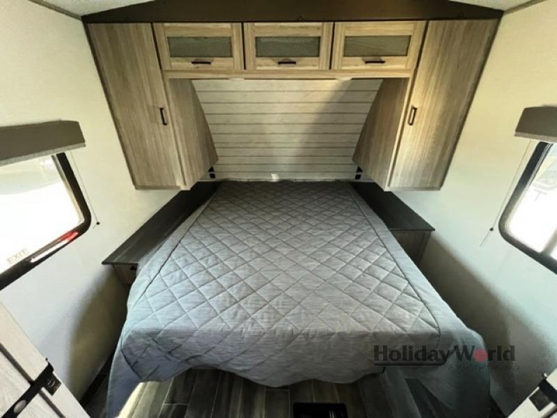 Cozy RV rental bedroom features a neatly made bed with a grey comforter, overhead cabinets, and side storage.. Keystone RV Passport GT 2022