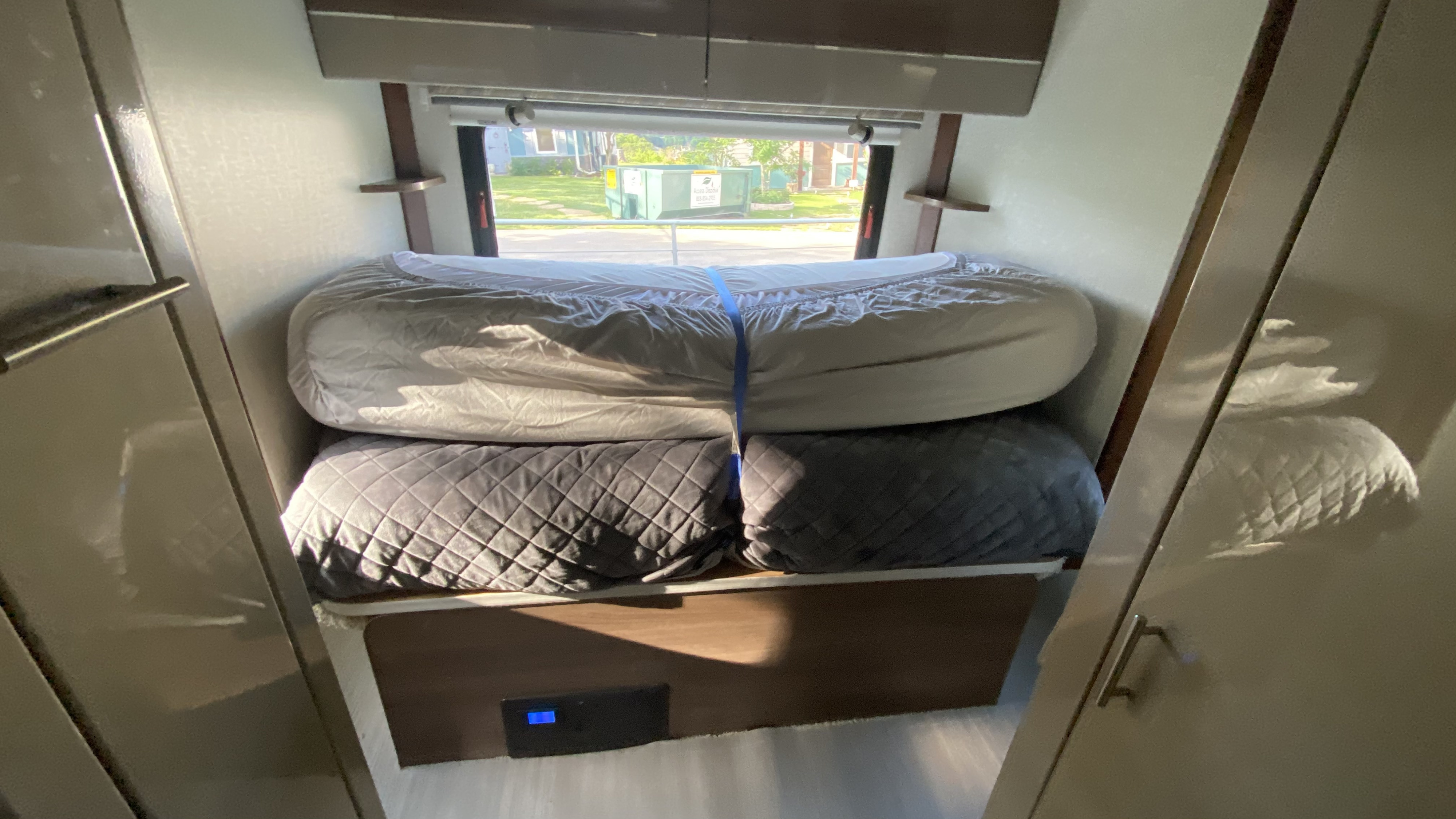 RV rental bed area with stacked, secured cushions, ready for use. A window offers a view to the outside.. Winnebago View 2015