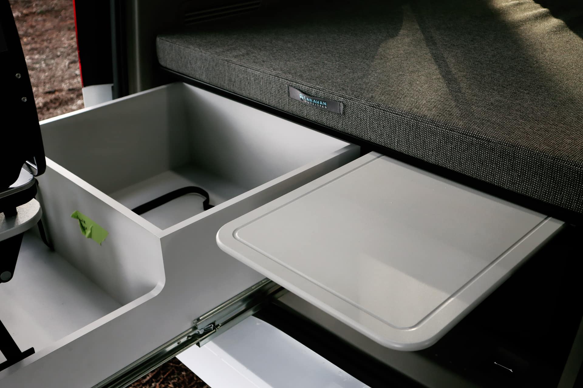 RV rental interior: A pull-out tray & open drawer next to a bed show smart storage in a compact camper.. Ford Transit Connect Wagon 2022
