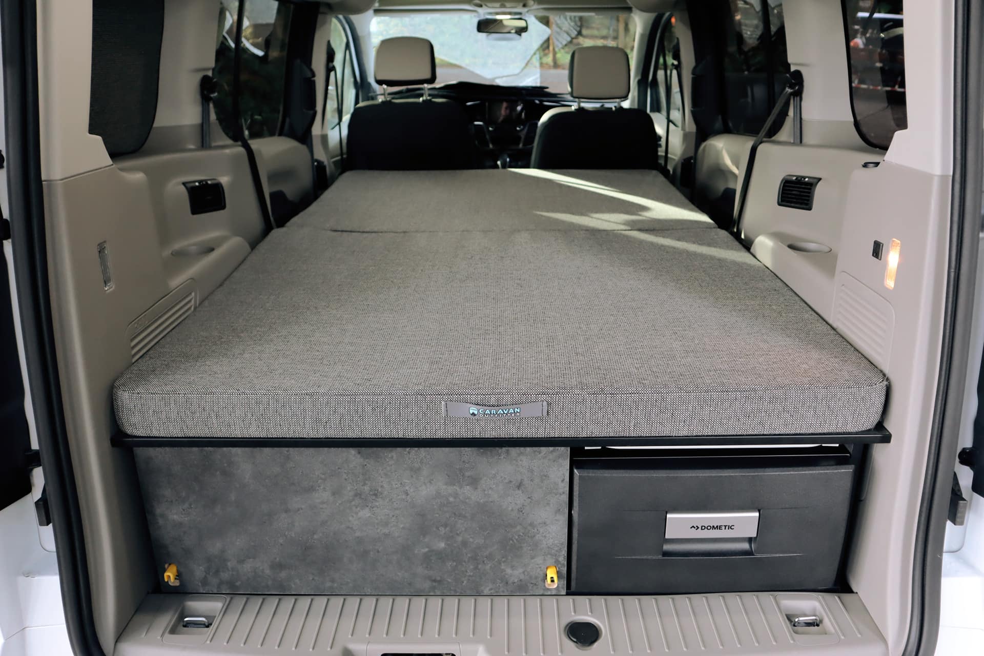 View inside an RV rental camper van, revealing a compact bed, under-bed storage, and Dometic cooler.. Ford Transit Connect Wagon 2022