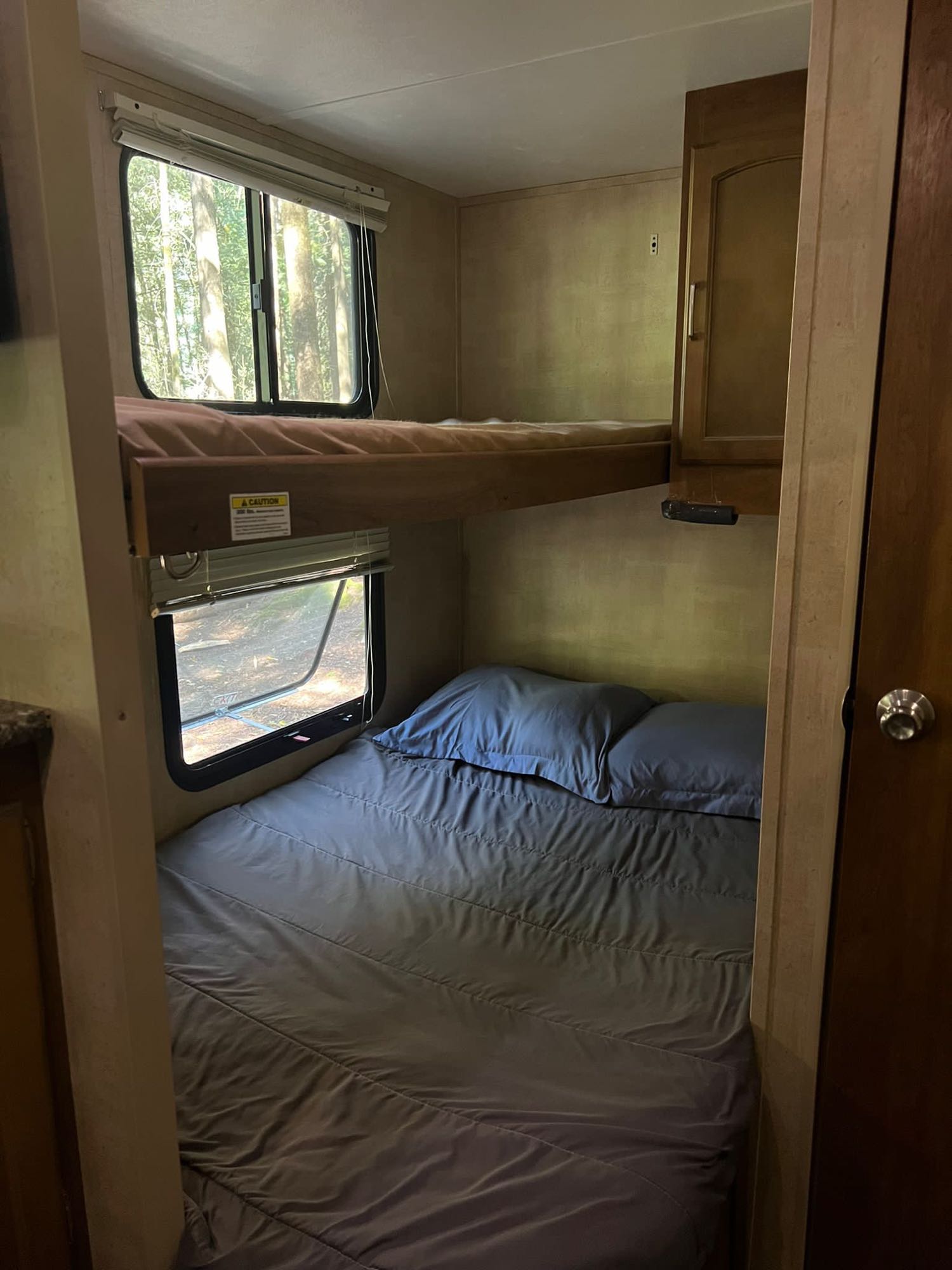 Inside the RV rental, twin bunk beds are made with fresh linens. Windows beside each bunk reveal lush green trees outside.. Keystone RV Springdale 2014