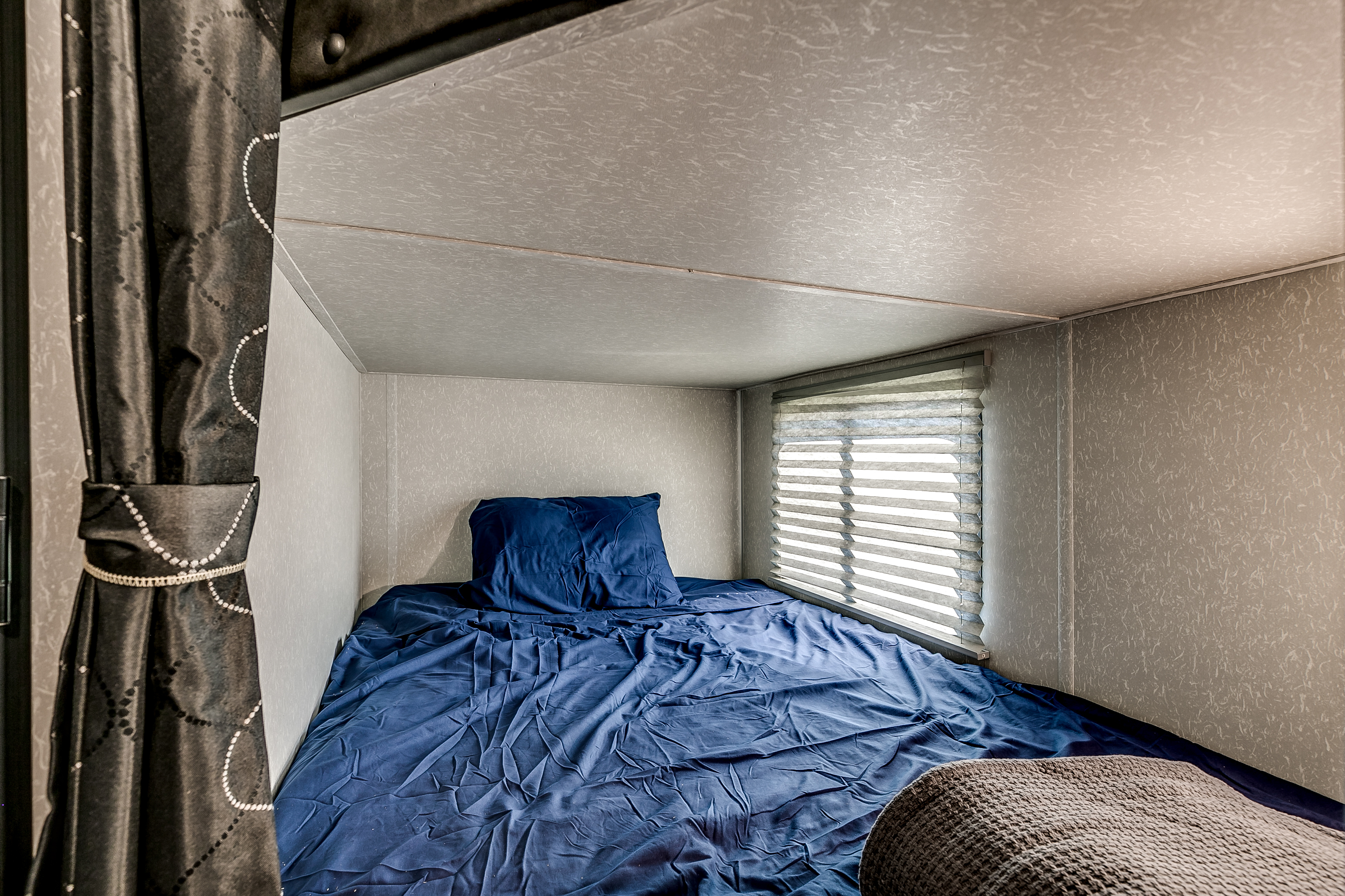 Cozy RV rental bunk with blue bedding and window blinds, offering a compact sleeping space.. Cherokee Grey Wolf 2022
