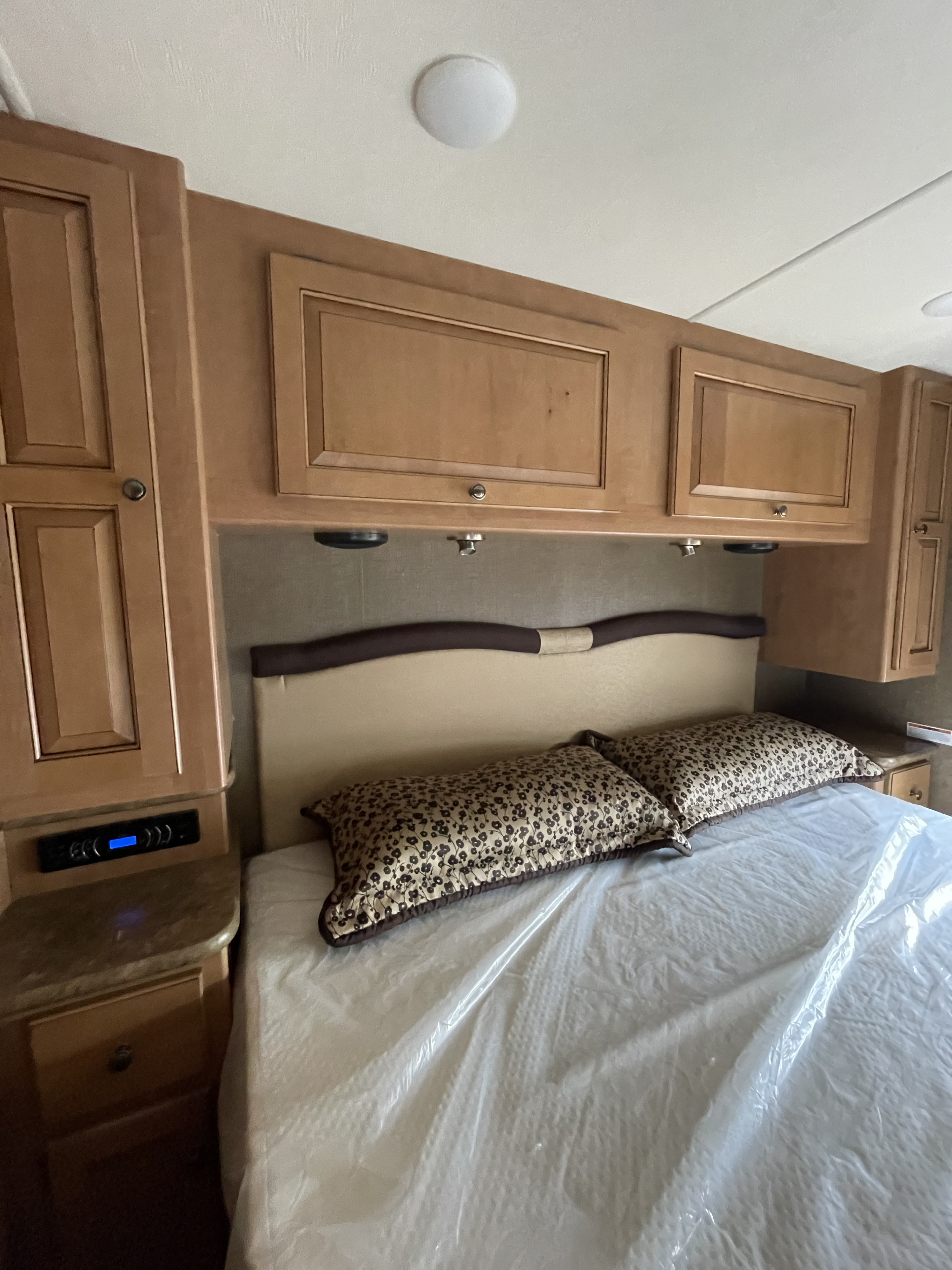 Experience comfort in this RV rental bedroom with warm wood overhead cabinets, a queen bed, and convenient side tables.. Thor Windsport 2016