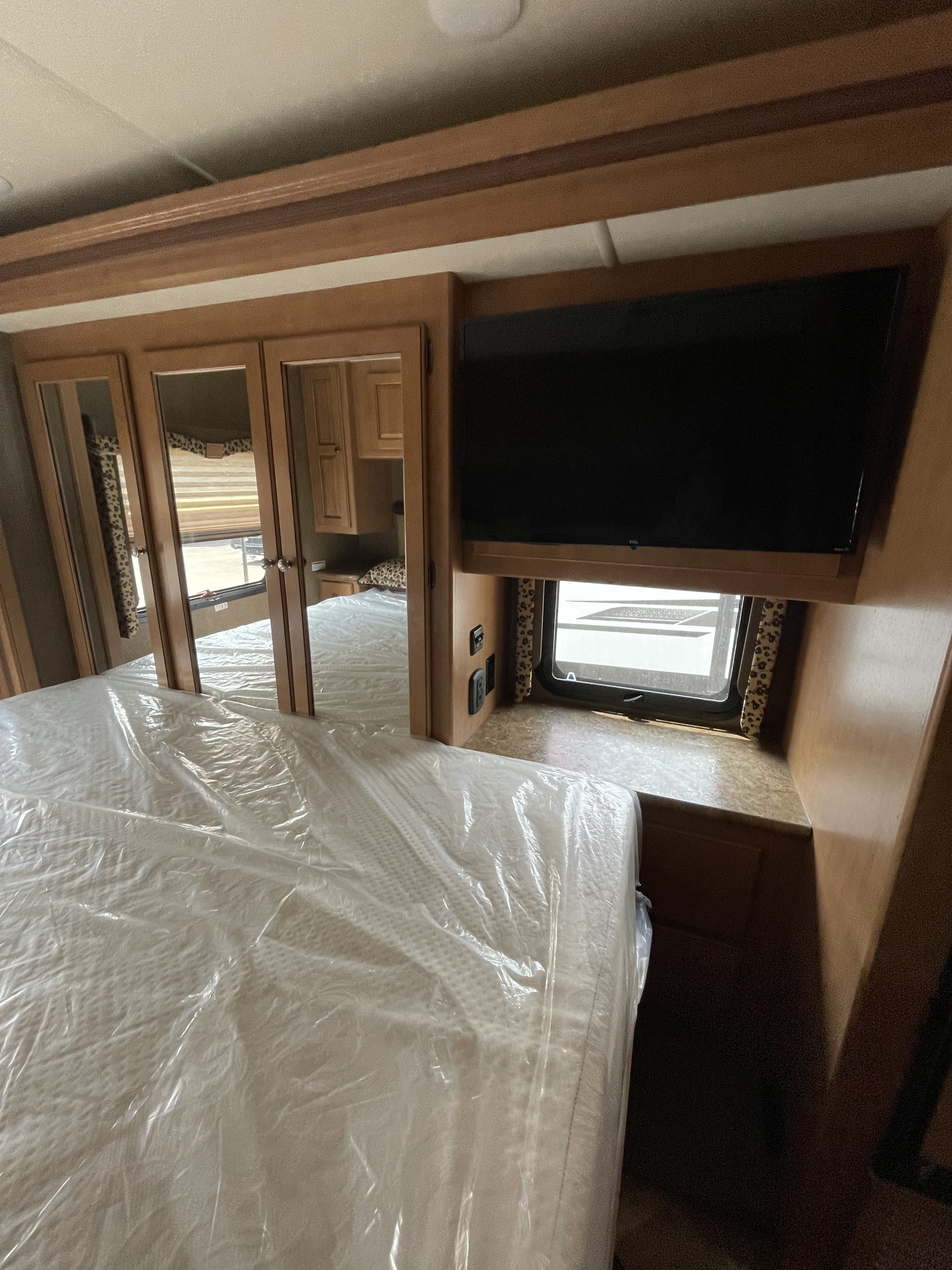 This RV rental bedroom features a plastic-covered bed, mirrored closet doors, and a mounted TV for your comfortable journey.. Thor Windsport 2016