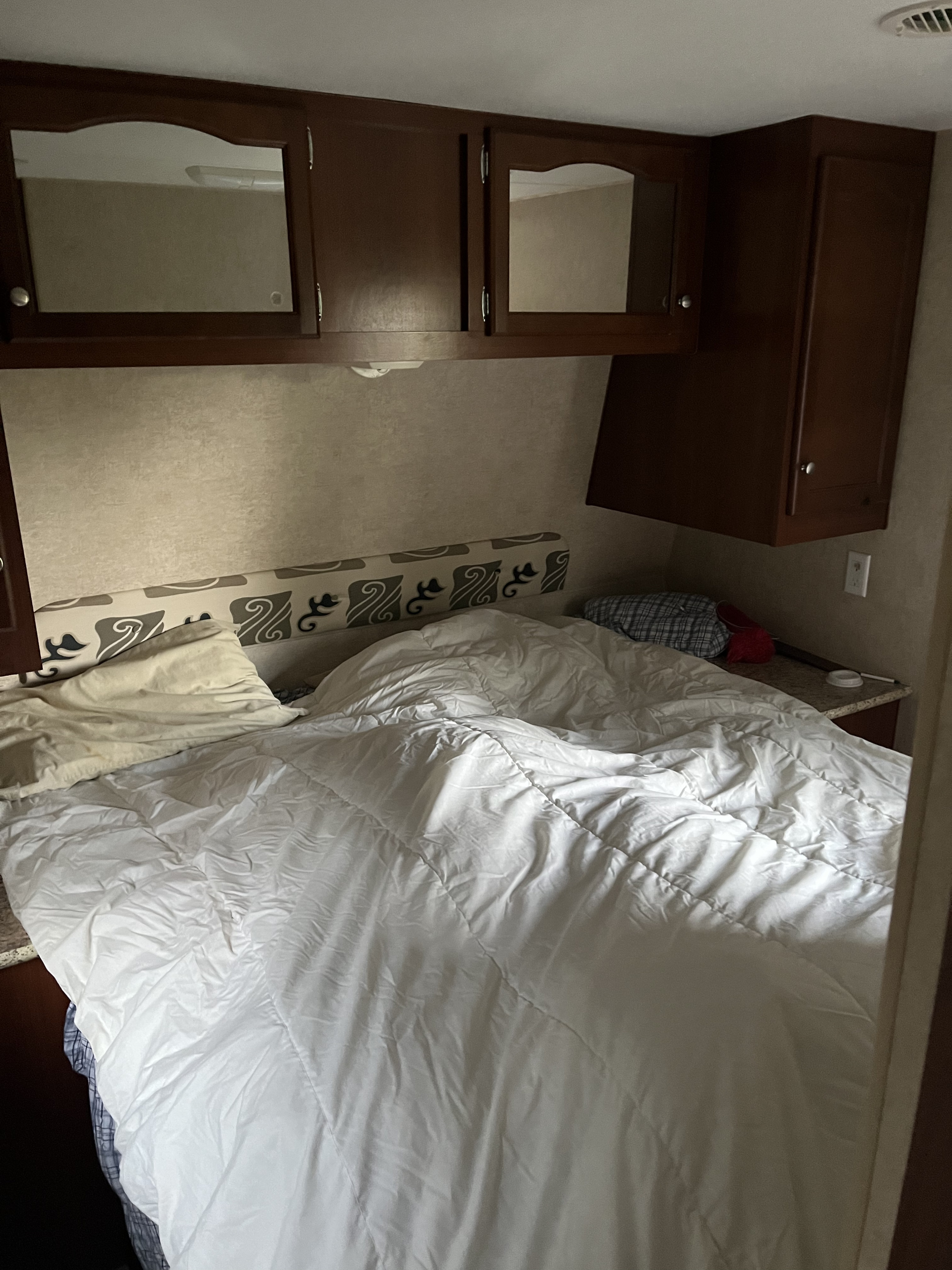 Cozy RV rental bedroom with rumpled white bedding, pillows, and dark wood overhead cabinets for storage.. Pioneer Pioneer Trailer 2009