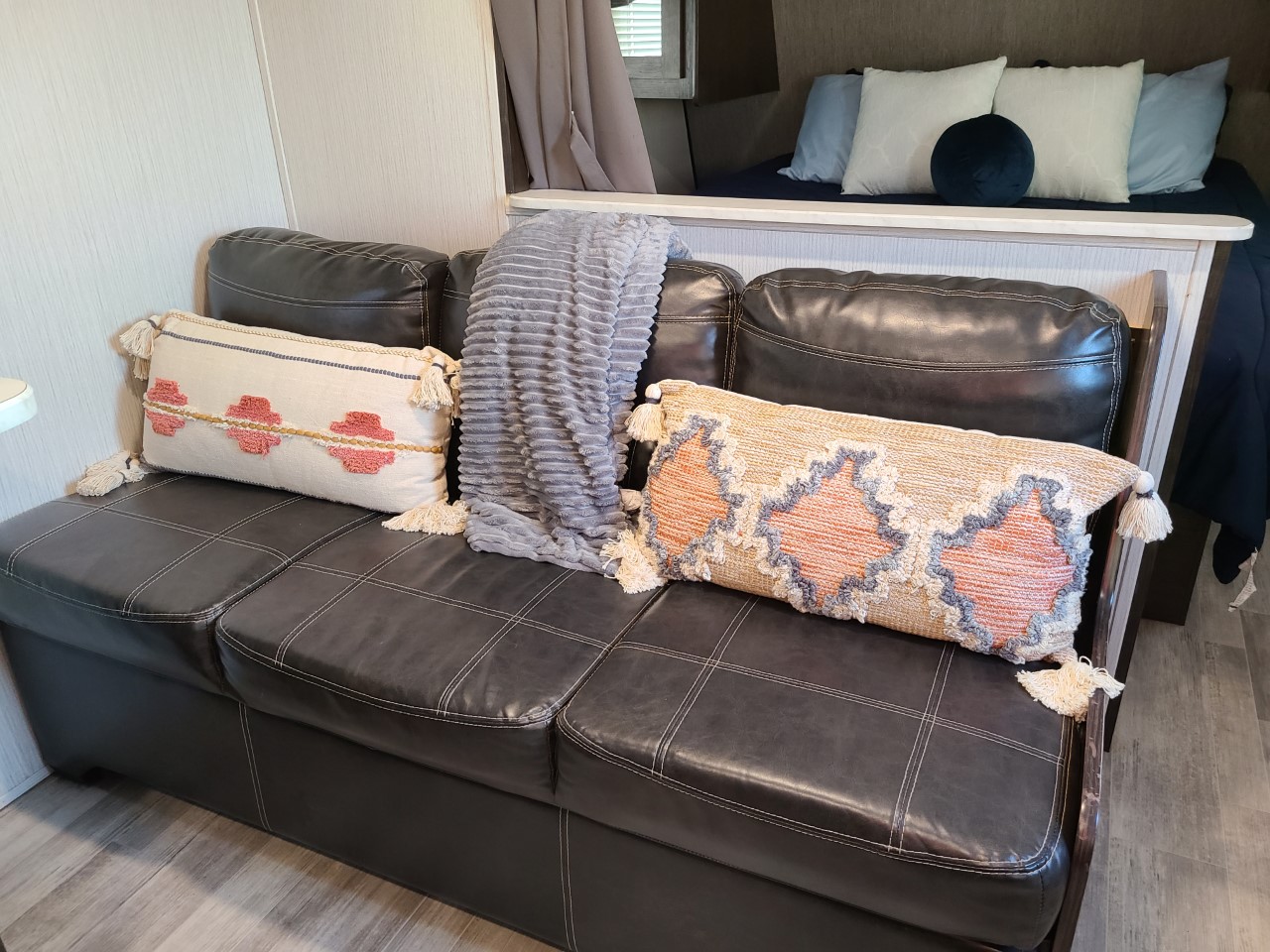 Cozy RV rental interior showing a dark leather sofa with decorative pillows and a blanket, next to a bed.. Heartland Prowler 2020