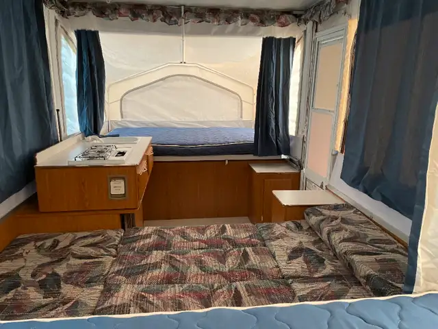 Pop-up RV rental interior featuring a main bed, compact kitchen with stove/sink, and convertible dinette/seating area.. Coachmen Clipper 2008