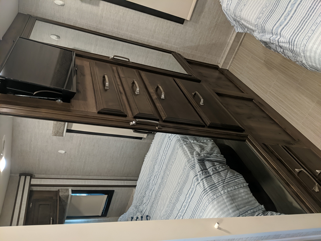 Inside an RV rental bedroom: dark wood cabinets, a mounted TV, and a cozy bed reflected in the mirror above.. Entegra Coach Esteem 2021