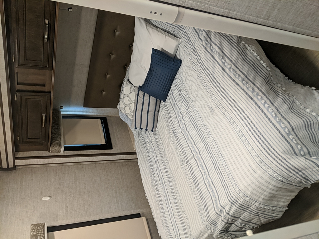 Experience comfort in this RV rental's inviting bedroom. Features striped bedding, tufted headboard, and wood cabinets.. Entegra Coach Esteem 2021