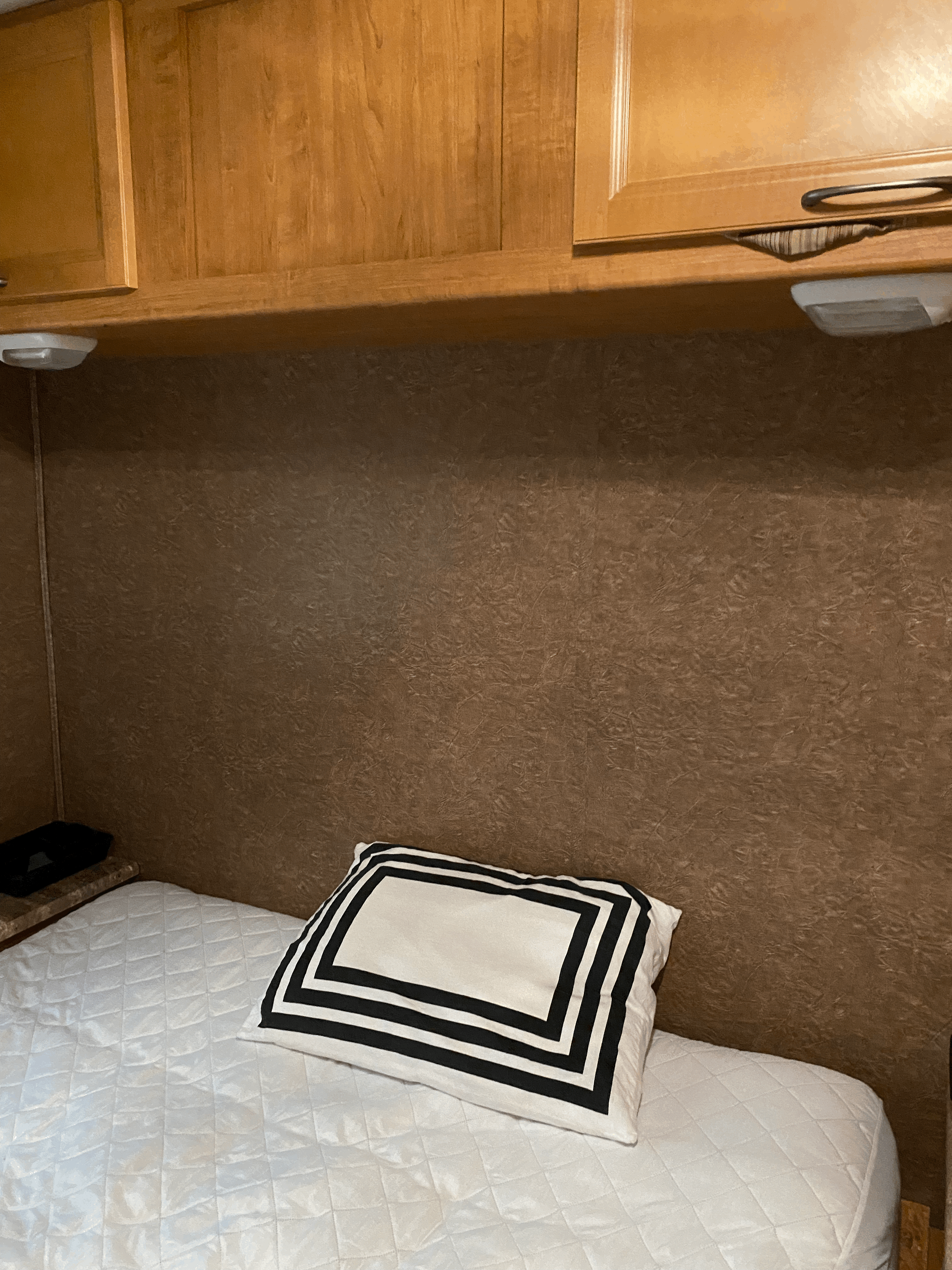 Relax in your RV rental! Cozy bedroom features a quilted bed, black/white pillow, & wooden storage cabinets.. Coachmen Pursuit 2015