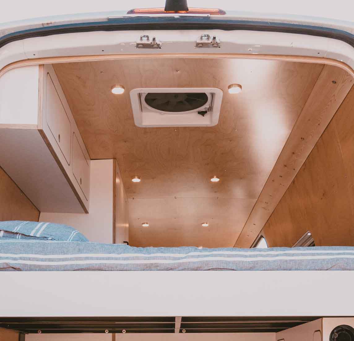 Cozy RV rental interior, viewed from the rear. Features a bed, wood ceiling with lights, fan, and storage cabinets.. Mercedes-Benz Sprinter 2022