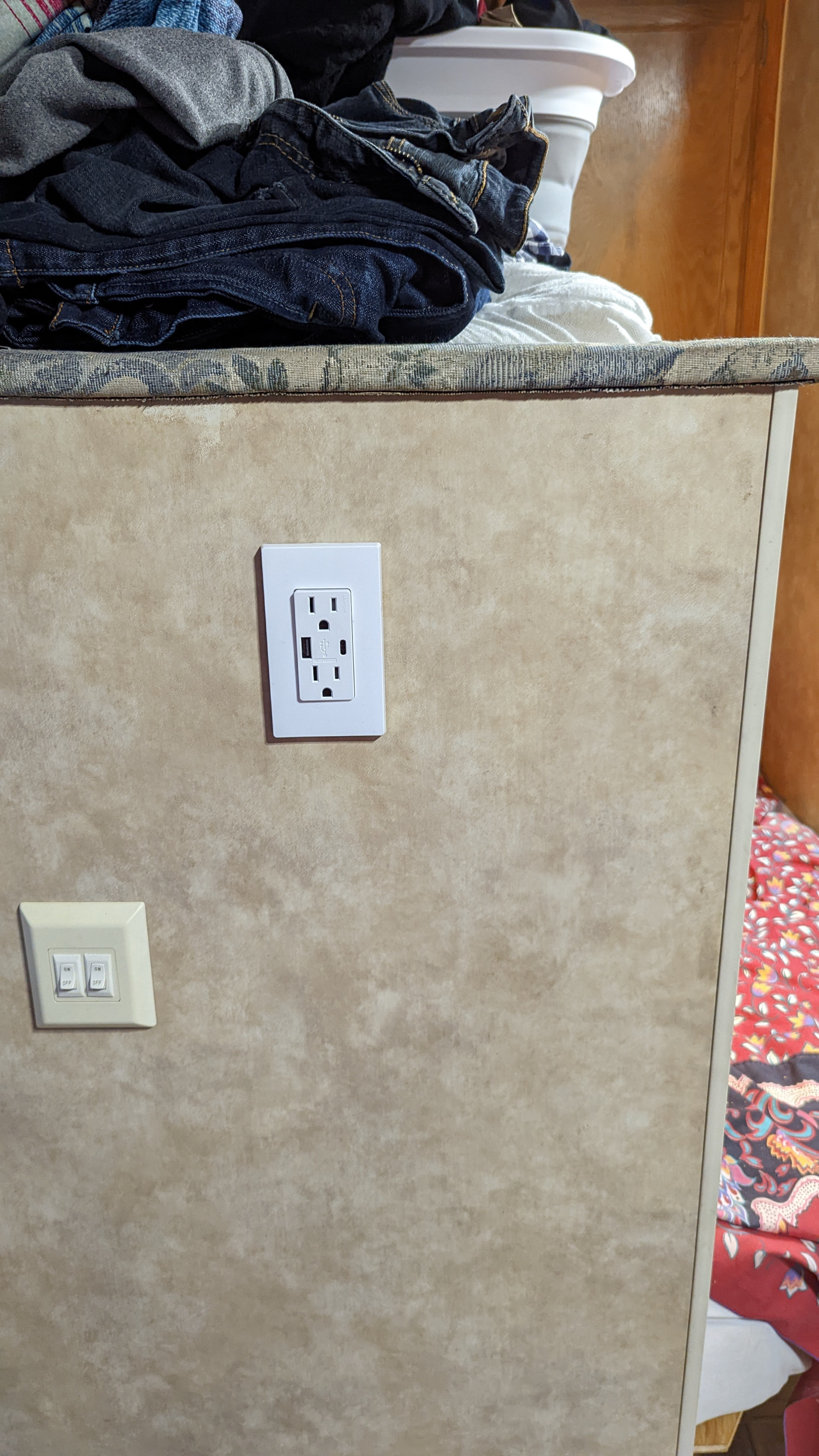 Inside an rv rental: Folded laundry on a counter, with an electrical outlet (featuring USB ports) and light switches on the wall.. Jayco Jay Feather Sport 2007