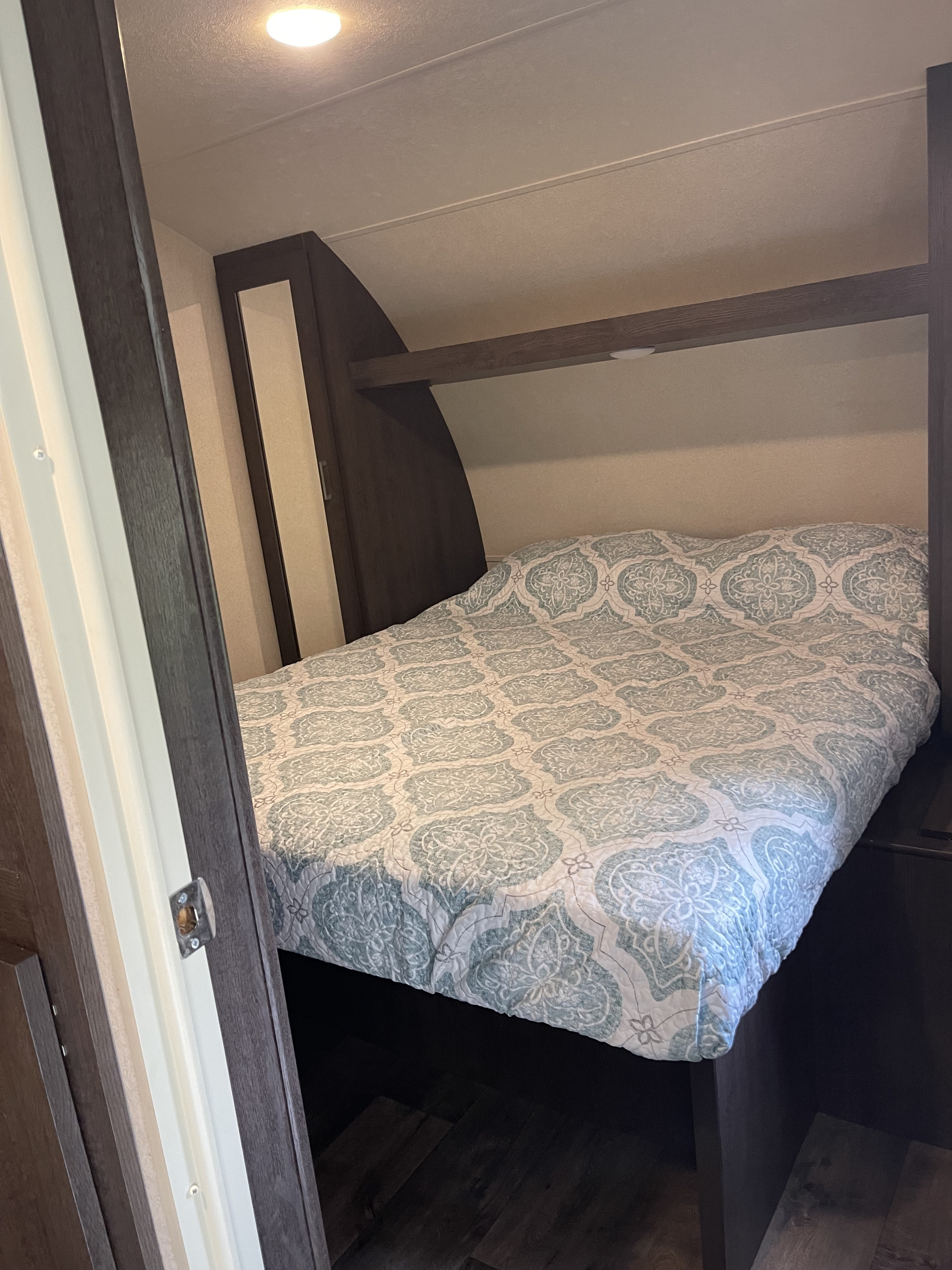 Compact RV rental bedroom with a bed featuring a light blue and white patterned quilt and dark wood finishes.. Forest River Salem 2018