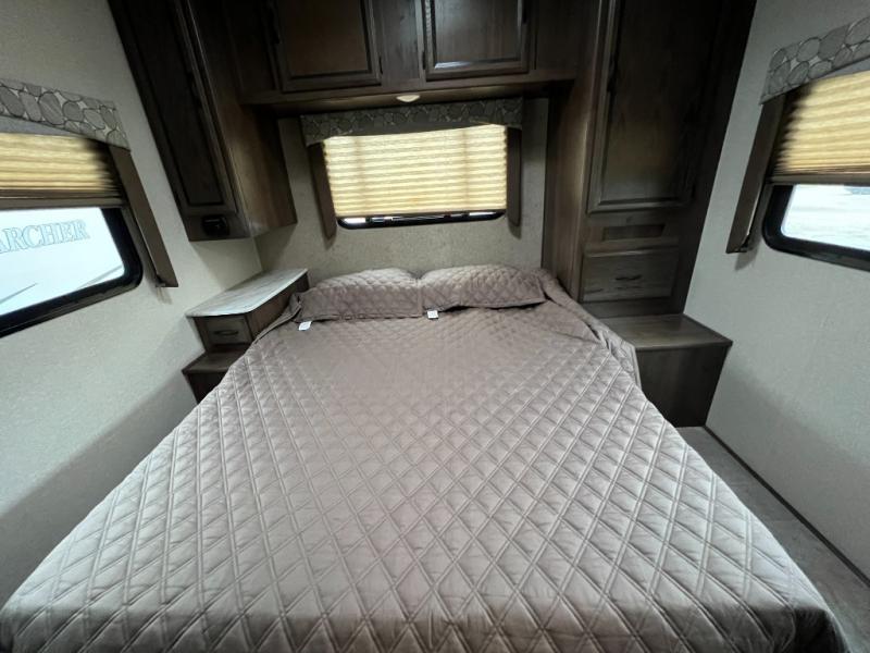 Cozy RV rental bedroom with a large quilted bed, dark wood cabinets, side tables, and window blinds.. Coachmen Freelander 2019