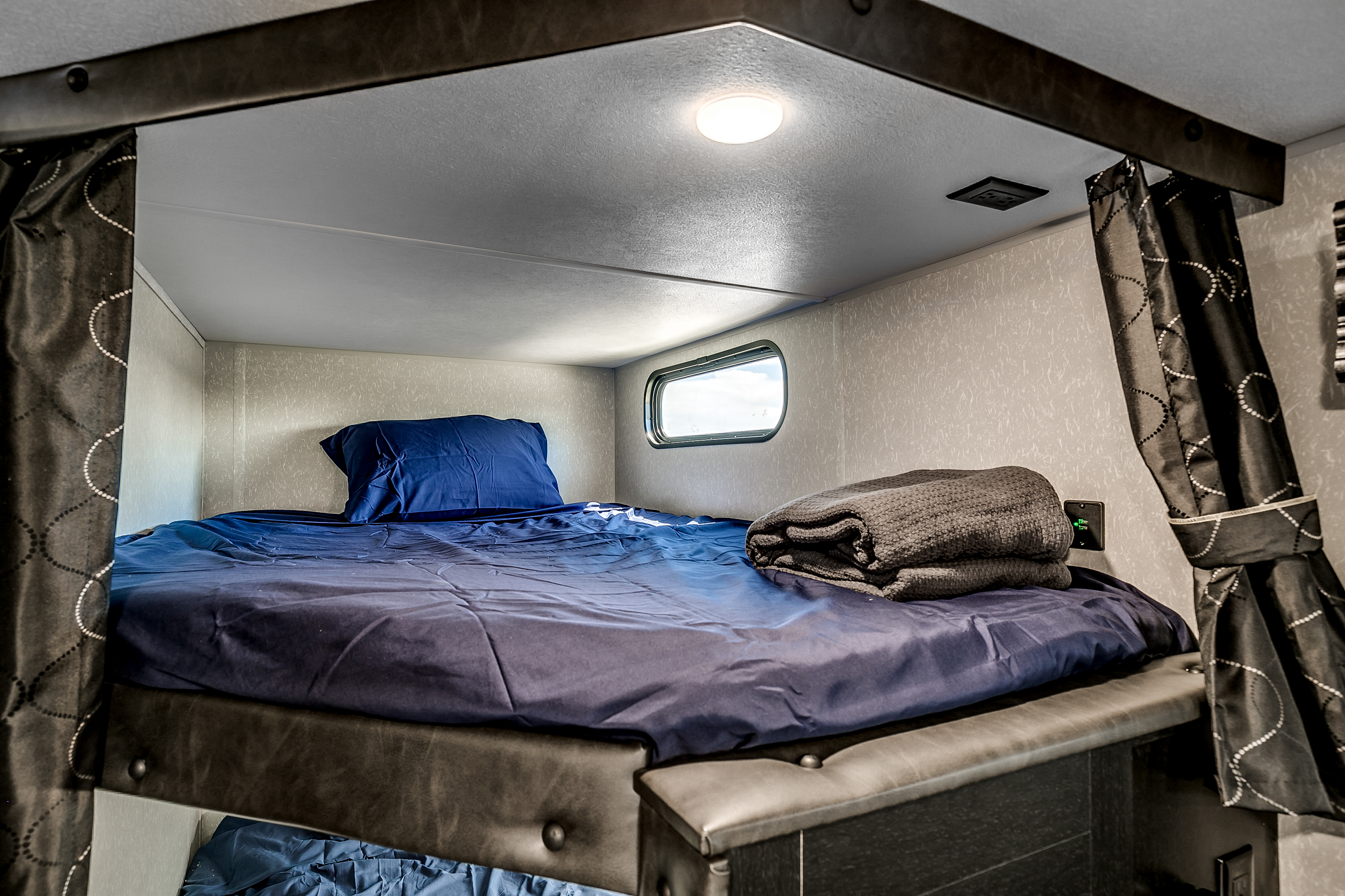 Cozy RV rental bunk beds with blue bedding, window, and curtain, offering a comfortable sleeping area inside.. Cherokee 26DBH 2022