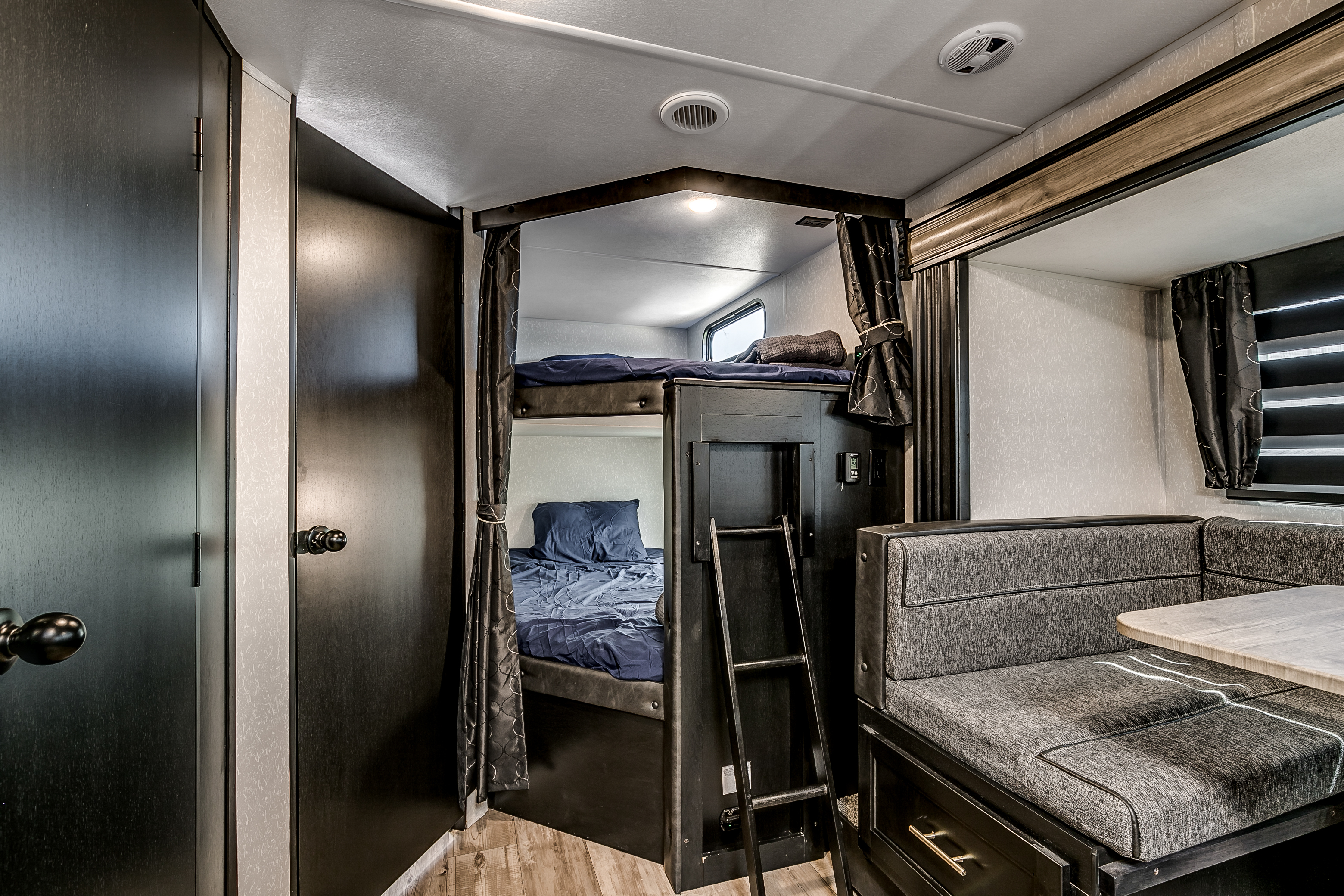 Cozy RV rental interior featuring private bunk beds with blue bedding, a ladder, and a functional dinette with grey seating.. Cherokee 26DBH 2022