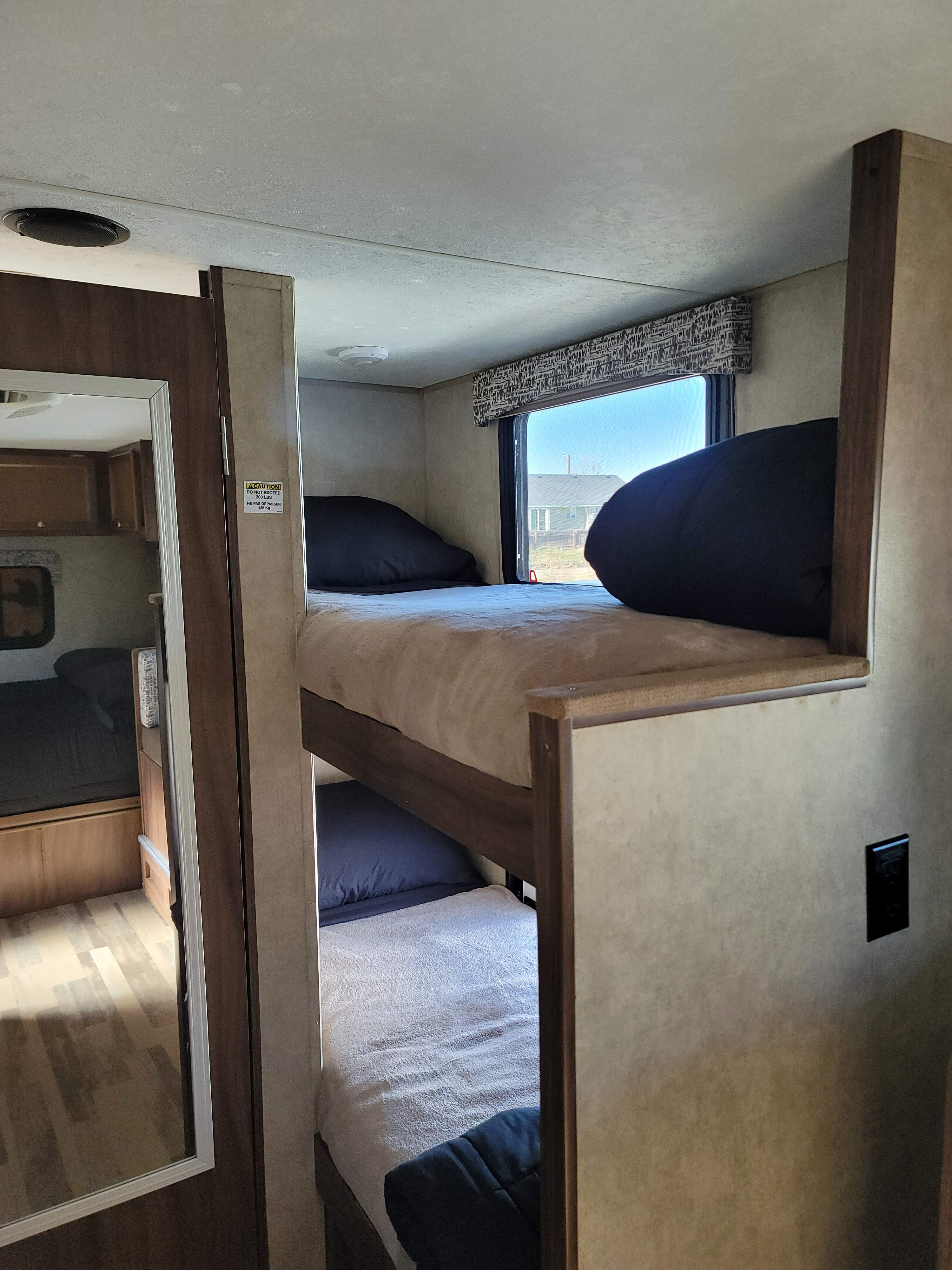 RV rental interior shows comfortable bunk beds with light bedding and black pillows. A window offers an outdoor view.. Forest River Viking 2018