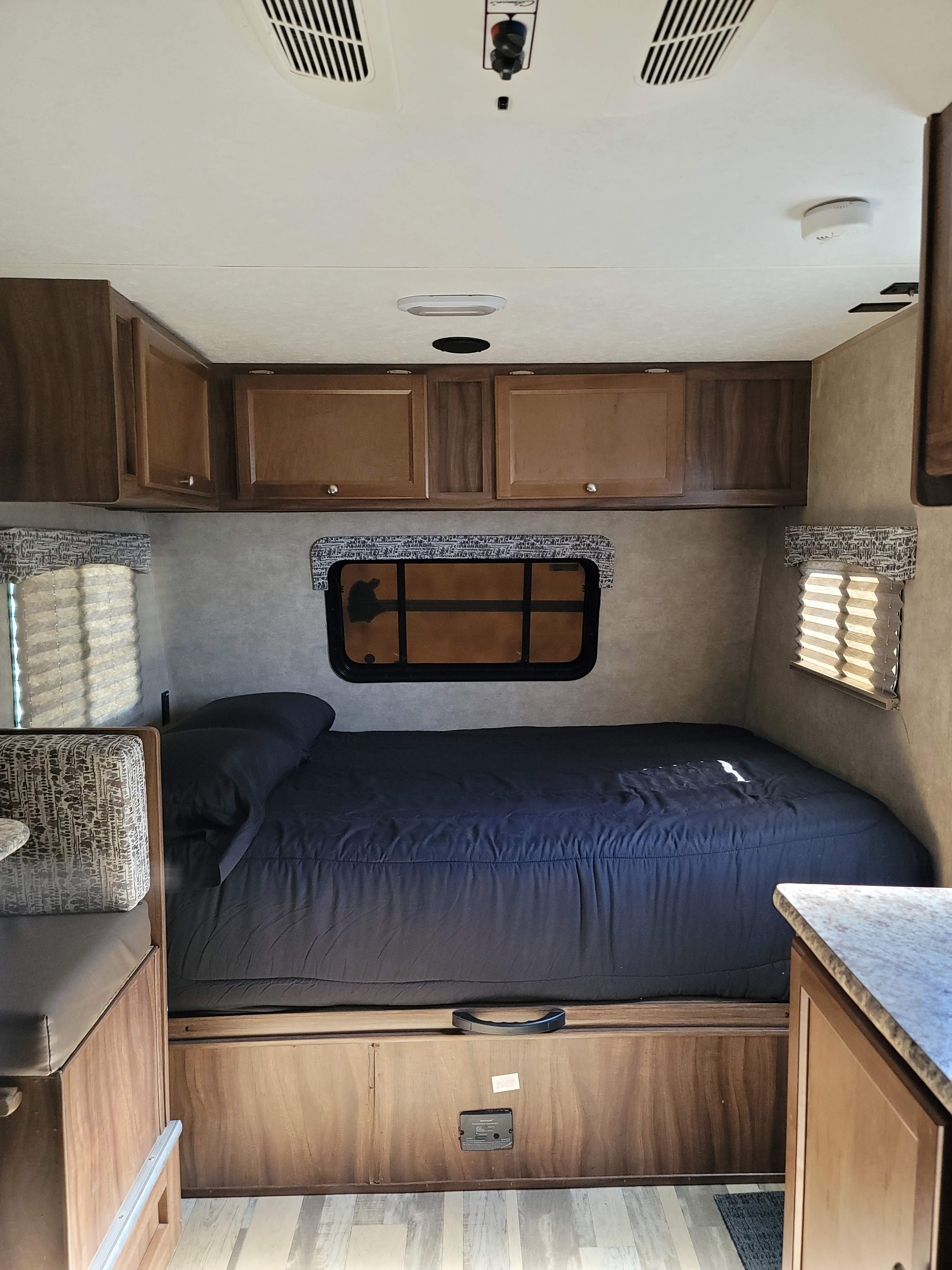 Compact **RV rental** bedroom and living area, featuring a dark bed, light wood cabinets, and a small dinette.. Forest River Viking 2018