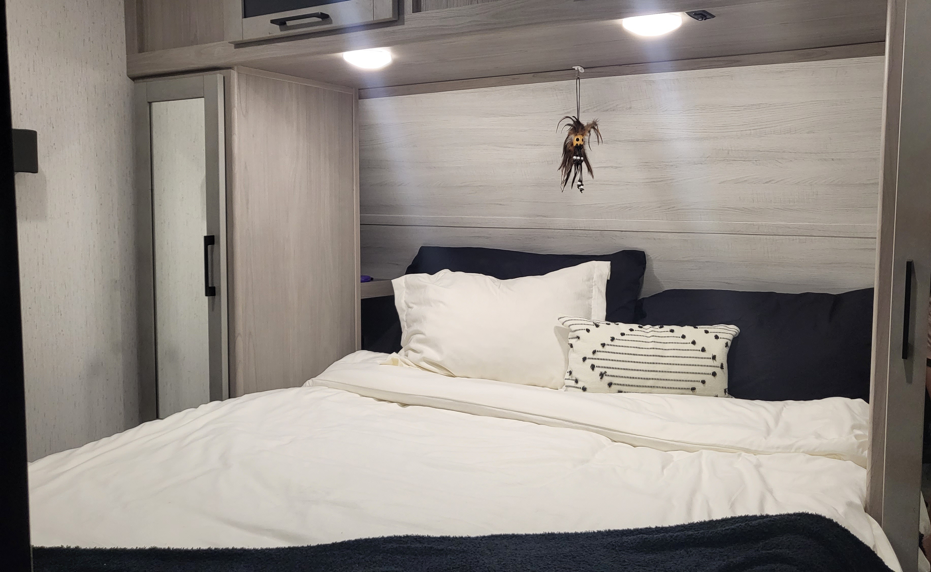Cozy RV rental bedroom featuring white bedding, black pillows, a mirrored cabinet, and overhead storage. Ideal for travel.. Dutchmen Kodiak Ultra Lite 2022