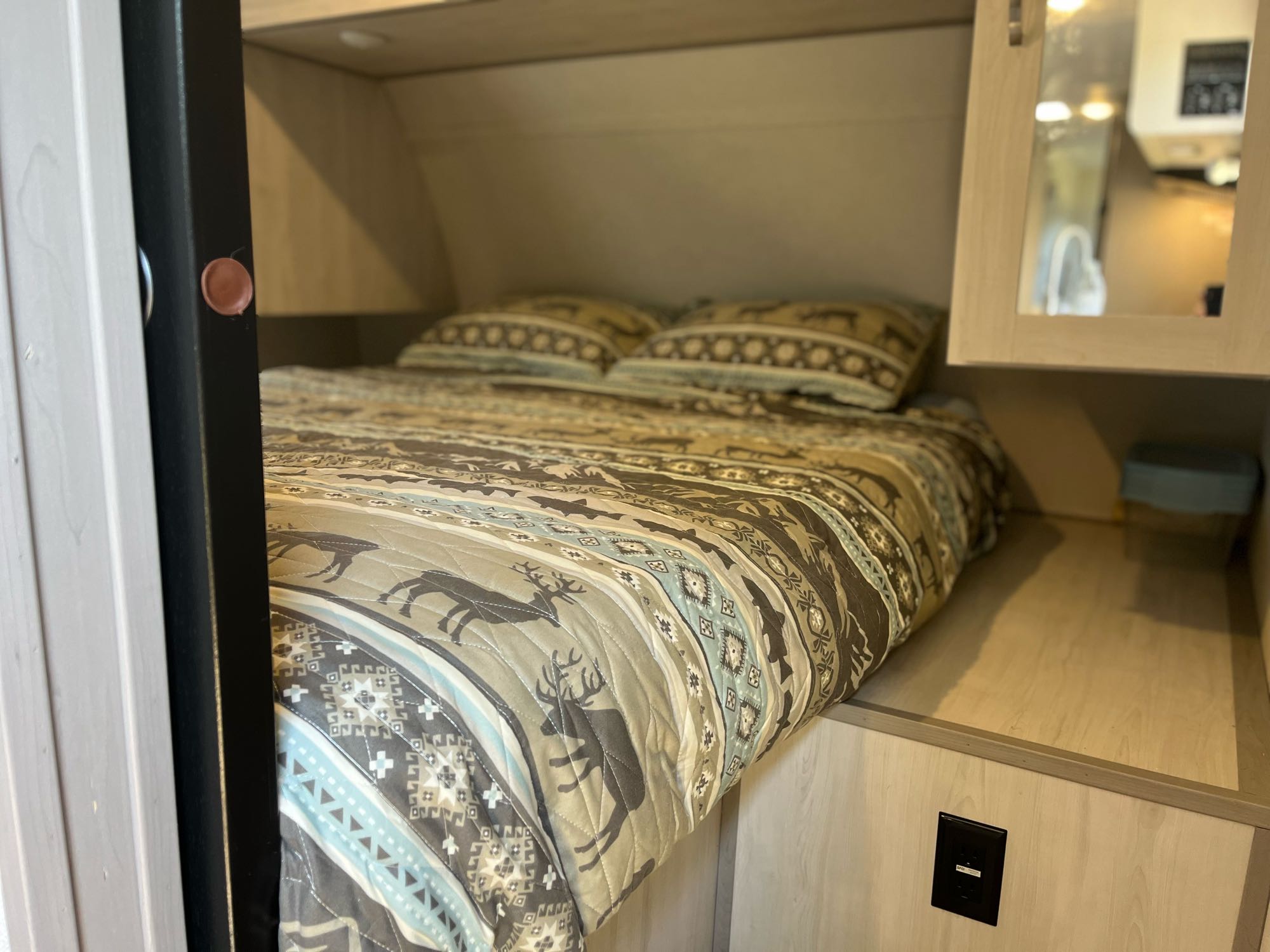 RV rental bedroom shows a bed with deer-patterned bedding & pillows, flanked by wood cabinetry with a mirror.. Forest River Tracer 2022