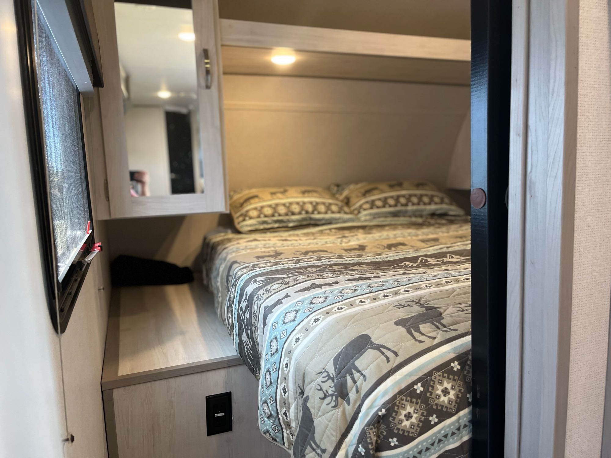 Cozy RV rental bedroom with a nature-themed bedspread, built-in storage, and a window, ready for travel adventures.. Forest River Tracer 2022