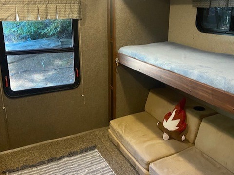 RV rental interior. Bunk beds and cozy sofa with a campfire pillow, next to a window showing outdoor scenery. Perfect for travel!. Heartland M-3385 2017