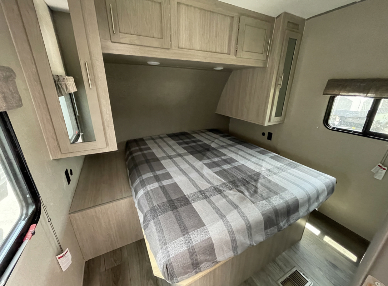 Modern RV rental bedroom: cozy bed with plaid comforter, ample overhead cabinets, and a side window.. Forest River Coachmen Catalina Legacy 2022