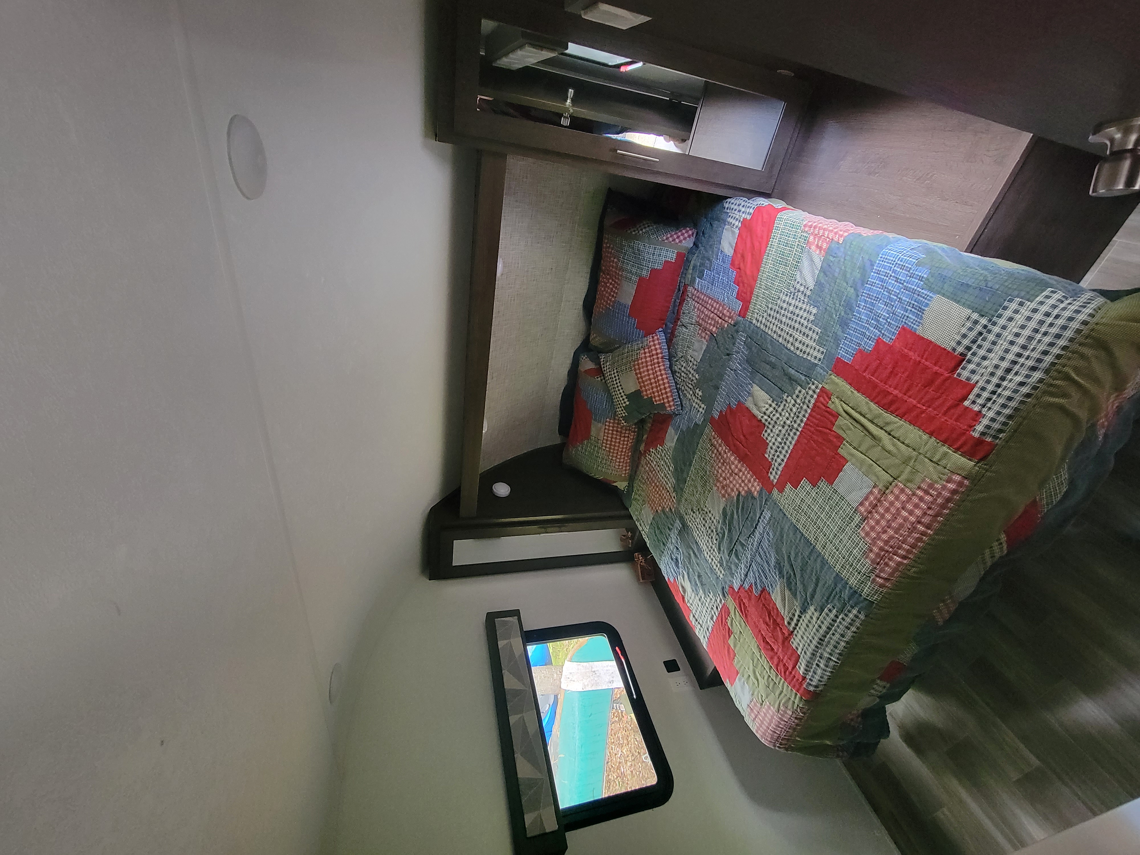 Cozy RV rental bedroom with a colorful quilt, overhead storage, and a window showing the outdoors.. Forest River Wildwood X-Lite 2019