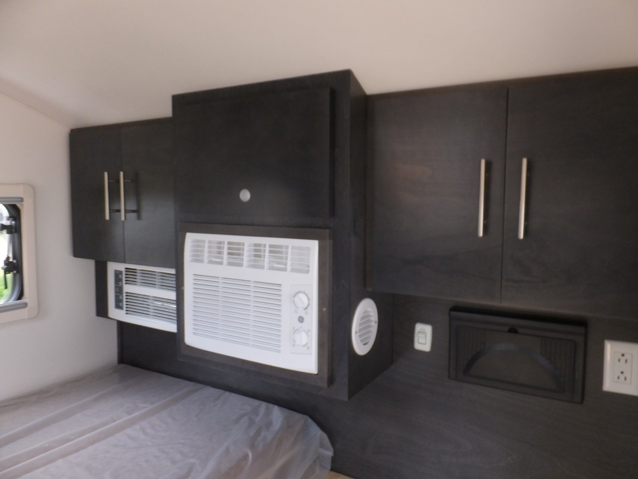 Compact RV rental interior featuring a bed, dark cabinetry, and two AC units for comfortable travel.. nuCamp T@G XL Boondock 2022