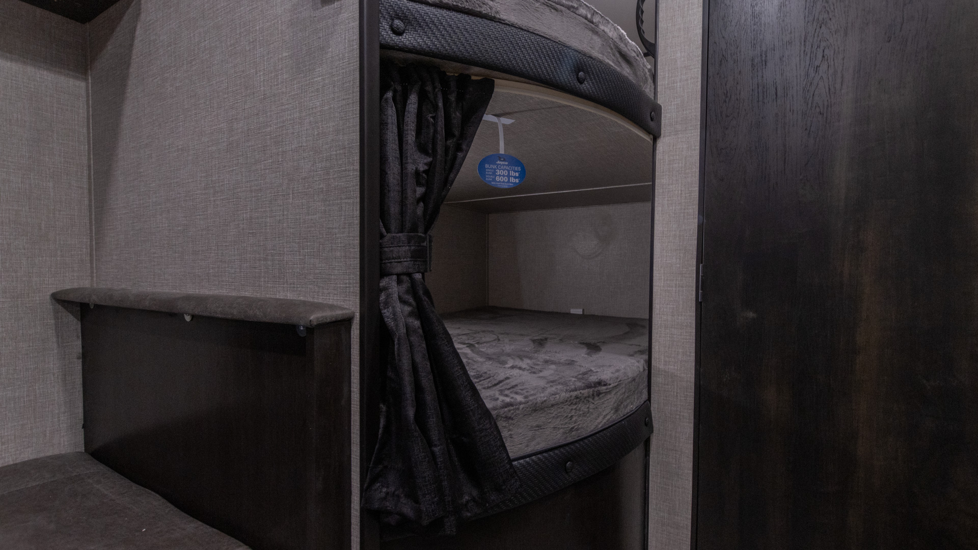Interior of an RV rental features cozy bunk beds with dark gray fabric walls and privacy curtains. Capacity tag: 300 lbs.. Jayco Jay Flight SLX 2022