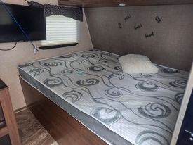 Cozy RV rental bedroom featuring a large, patterned mattress, white pillow, and wall-mounted TV. Ideal for your travel adventures.. Heartland RVs Pioneer 2018