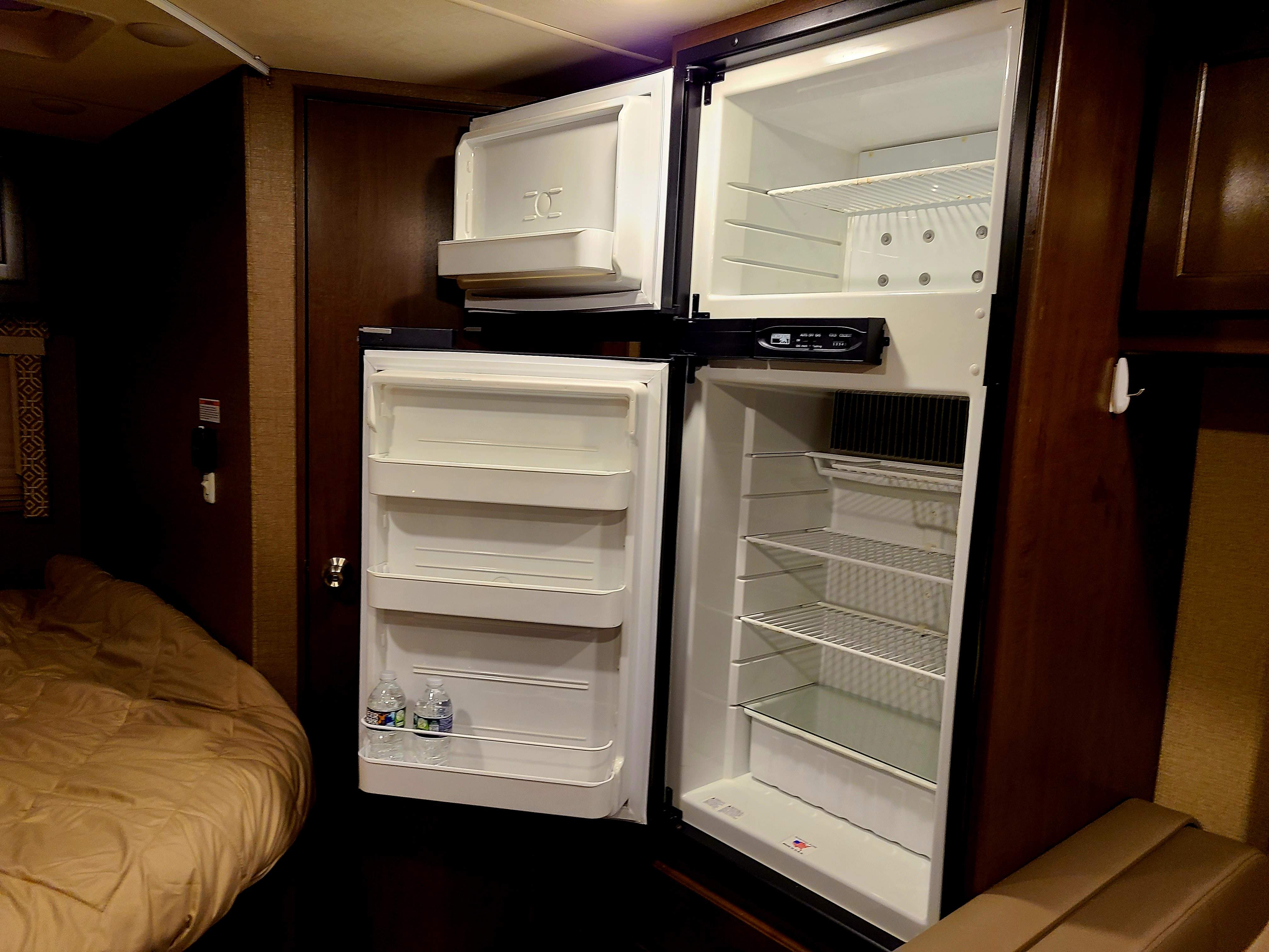 Check out the spacious refrigerator in this RV rental! The open fridge and freezer show ample storage next to a comfy bed.. Thor Freedom Elite 2018