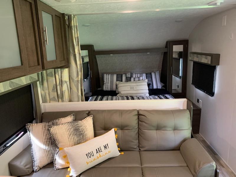 Modern RV rental interior showcasing a cozy bed & couch. Ideal for comfortable road trip travel & camping.. Forest River Wildwood X-Lite 2019