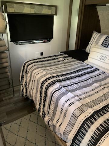 Inside a modern rv rental bedroom: a comfy bed with black/white stripes, wall-mounted TV, and cozy rug.. Forest River Wildwood X-Lite 2019