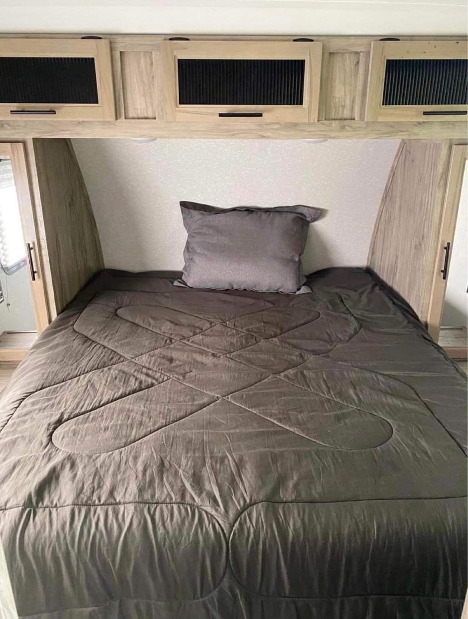 Compact RV rental bedroom: bed with grey bedding, overhead storage, and wood-look panels. Cozy interior for travel.. Forest River Cherokee 2022