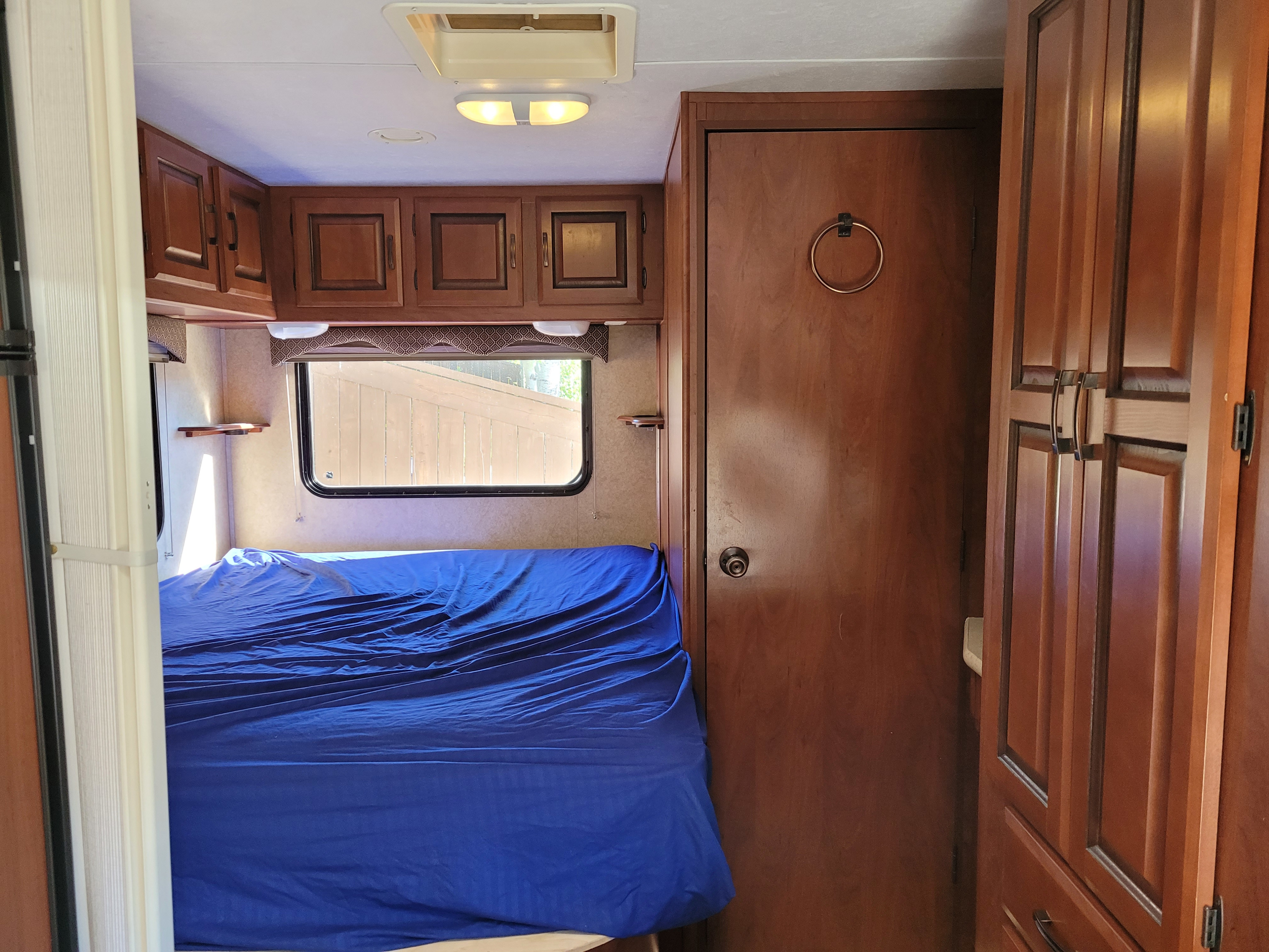 RV rental interior: bedroom with a blue-covered bed, wood cabinets, windows, and a closed door on the right.. Forest River Sunseeker 2011