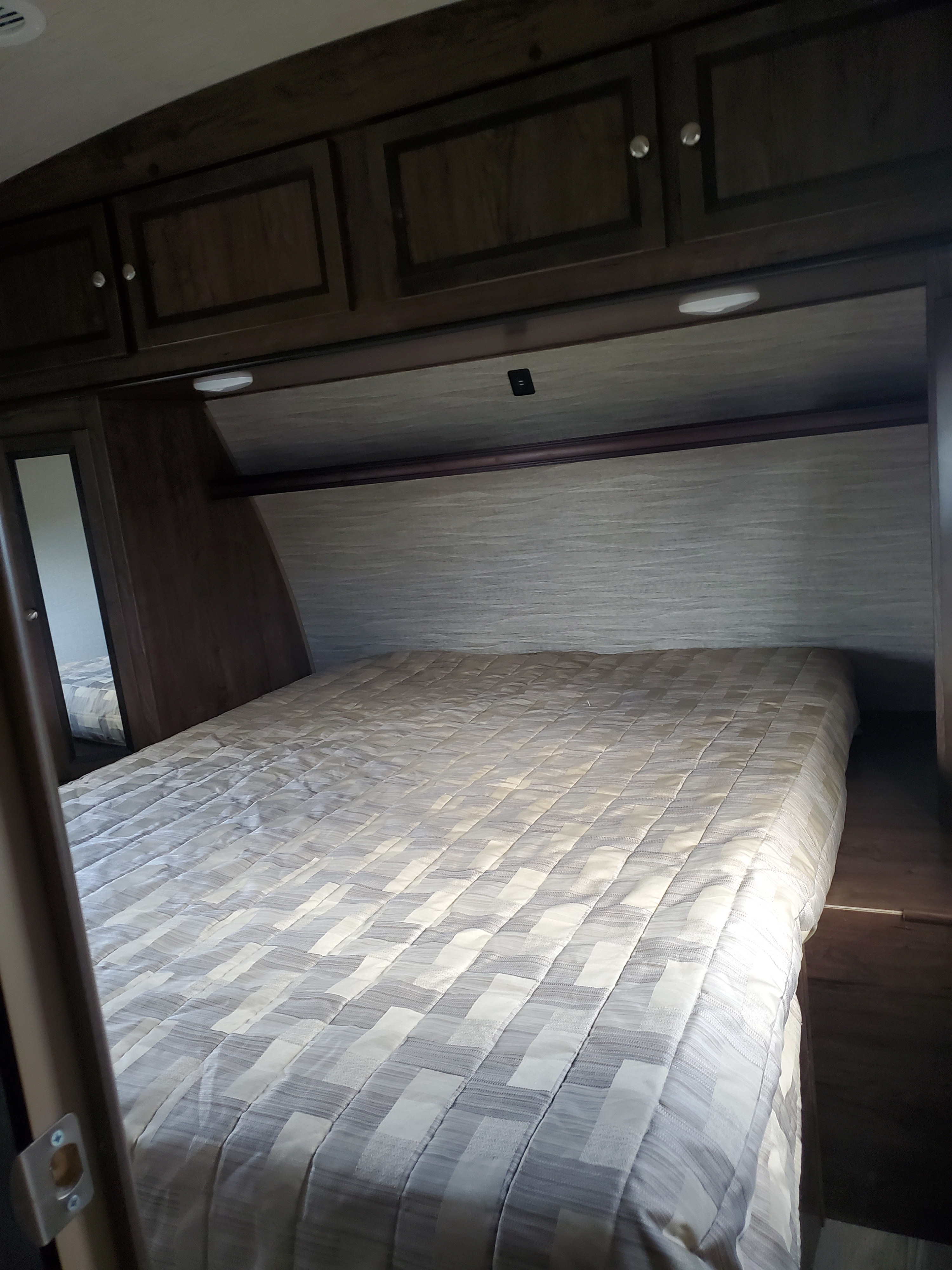 RV rental bedroom: Compact space featuring a patterned comforter, dark wood cabinets, and a built-in mirror.. Cruiser RV MPG Ultra Lite 2018