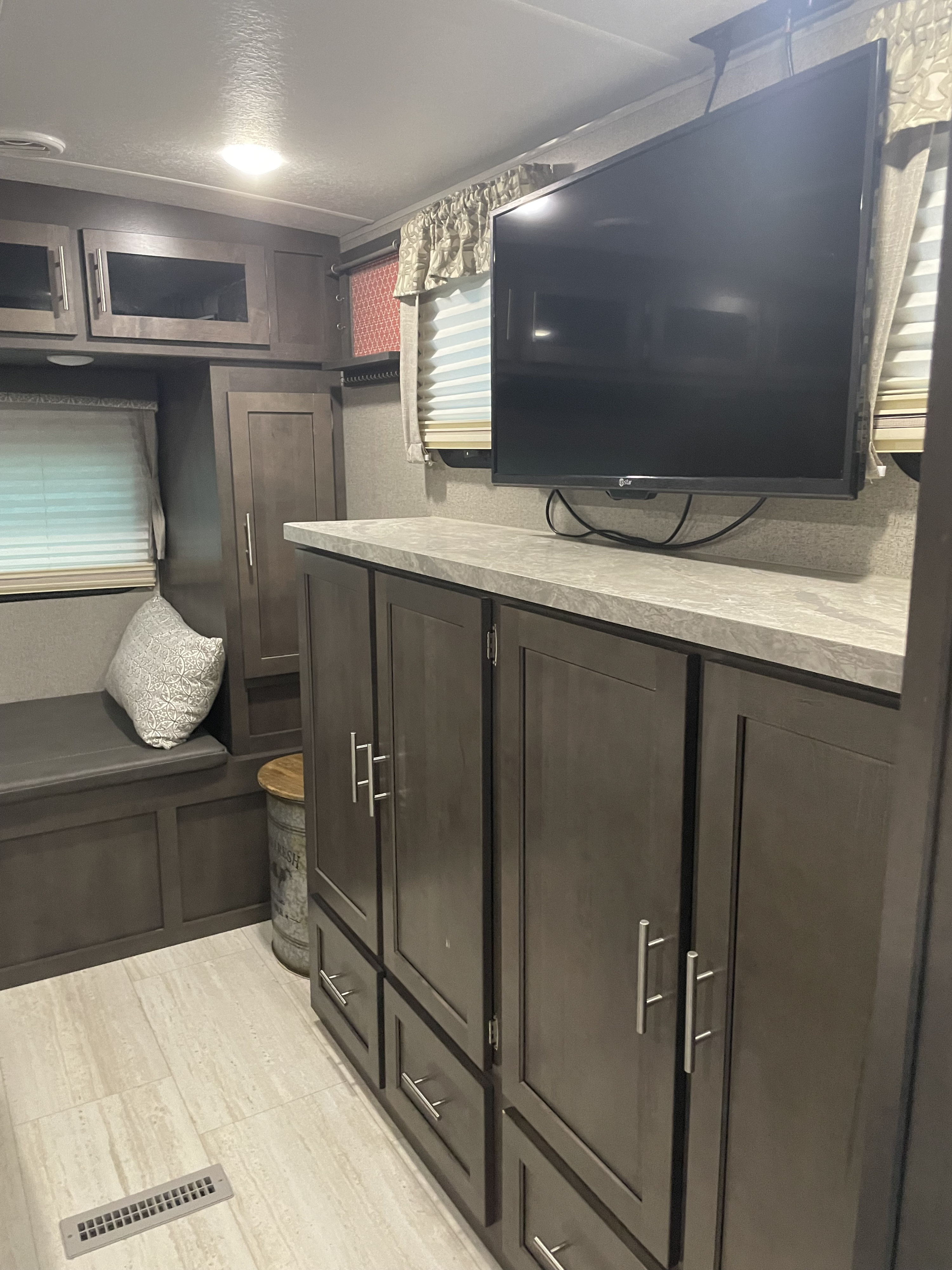 RV rental living area with a mounted TV, storage cabinets, counter, built-in bench, and patterned pillow, showcasing a cozy space.. Forest River Rockwood Ultra Lite 2020