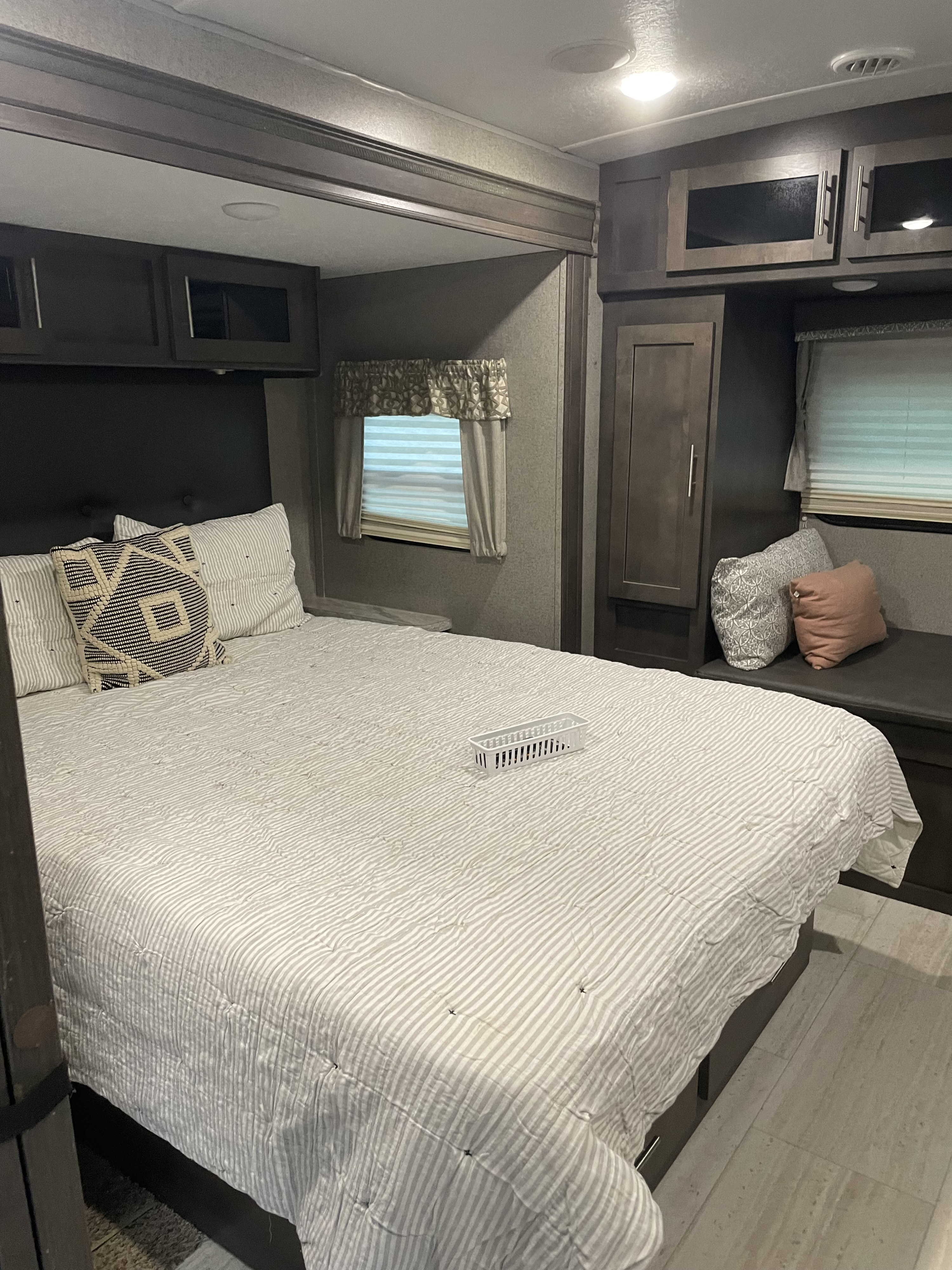 Experience comfort in this RV rental bedroom: striped bed, storage cabinets, window, and cozy bench seating.. Forest River Rockwood Ultra Lite 2020