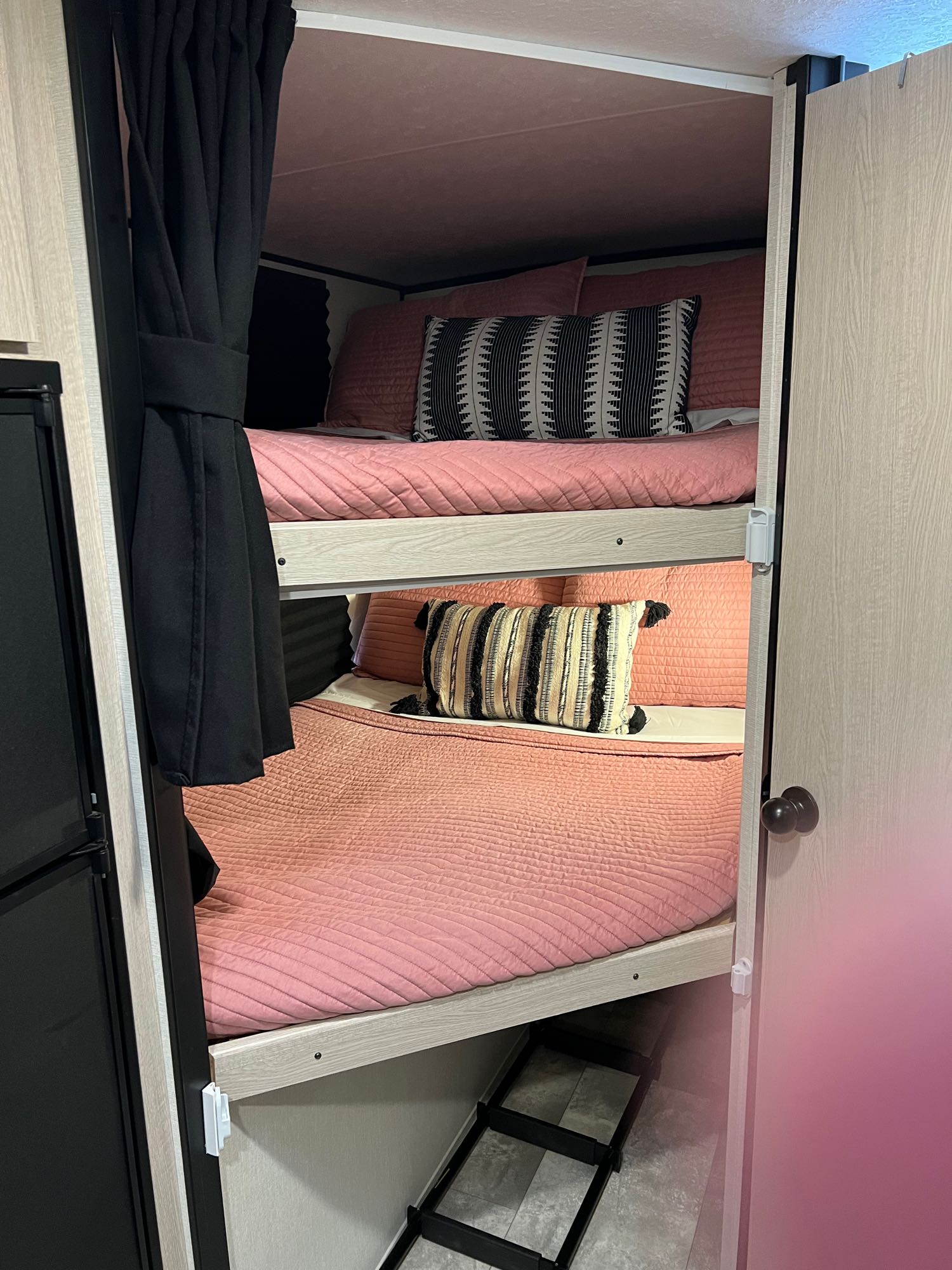 Cozy RV rental bunk beds feature pink bedding, decorative pillows, a privacy curtain, and ladder.. Coachmen Apex Nano 2022