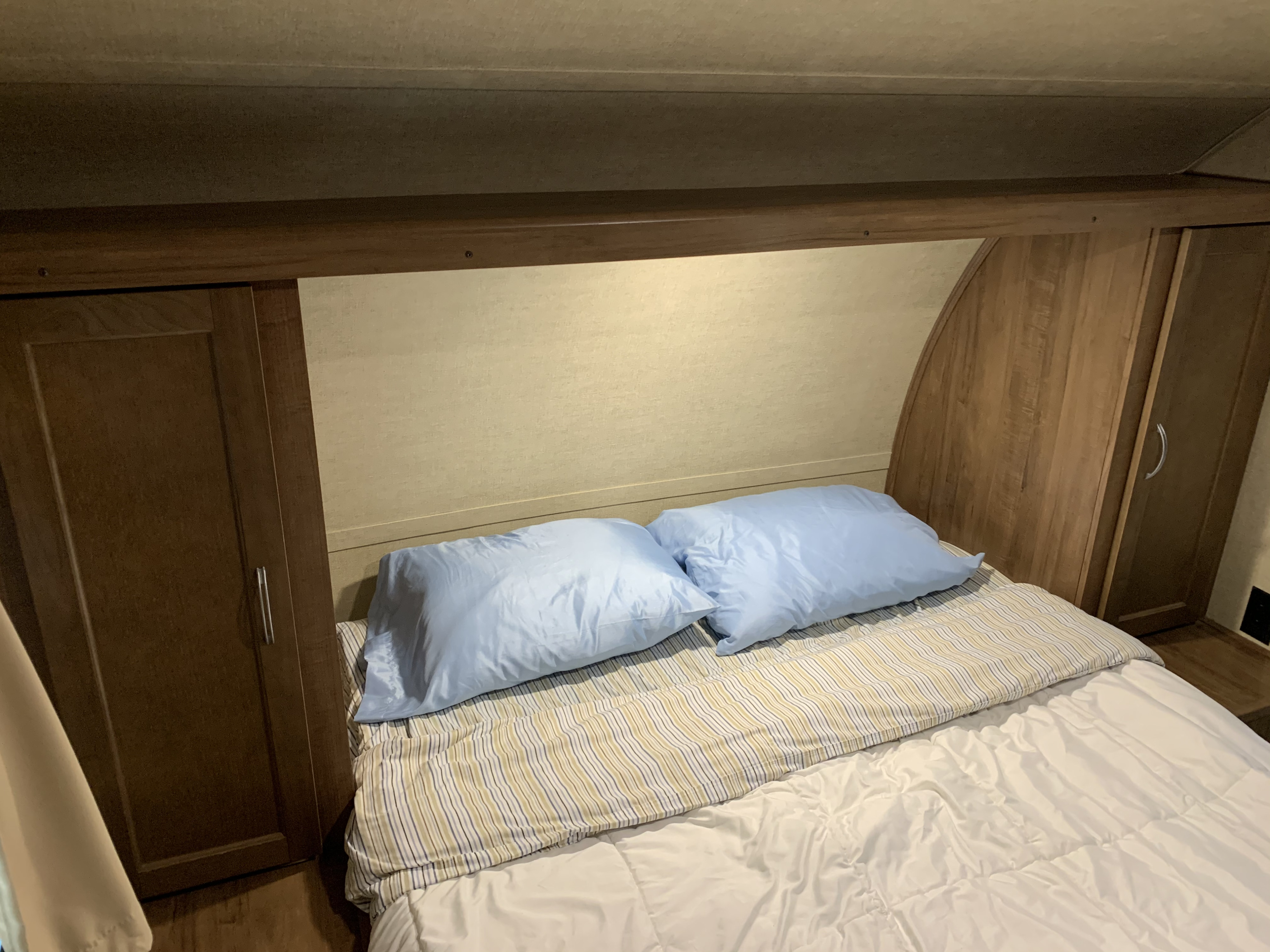 Cozy RV rental bedroom with light blue pillows, striped bedding, and built-in wood cabinets, offering a compact sleeping area.. Gulf Stream Conquest 2019